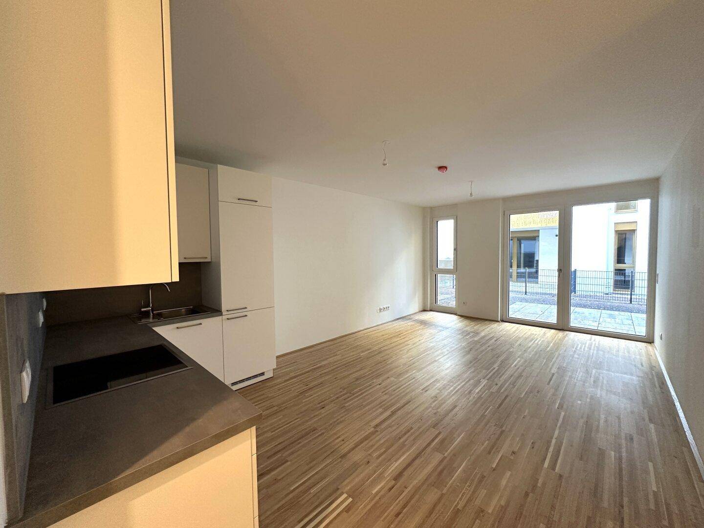 Heller Wohnbereich mit Parkettboden und großen Fenstertüren, die viel Tageslicht hereinlassen und Zugang zur Terrasse bieten.
