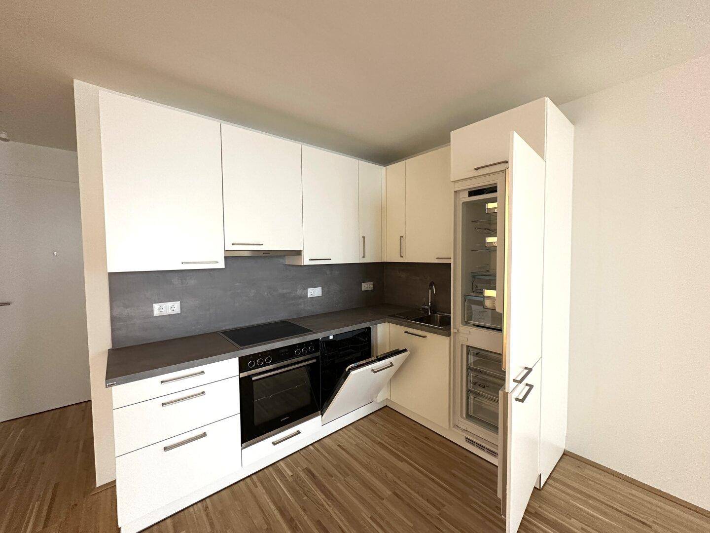 Moderne Einbauküche mit offenem Kühlschrank, weißen Fronten und integrierten Geräten für effizientes Kochen.