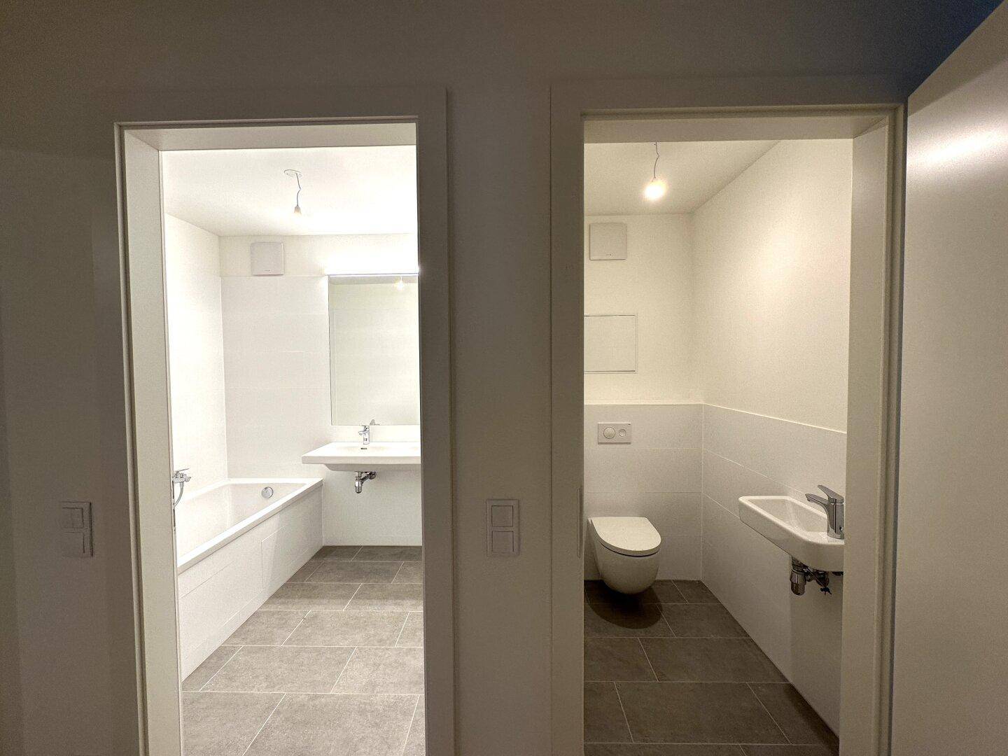 Flur mit Blick auf ein modernes Badezimmer mit Badewanne und eine separate Gästetoilette.