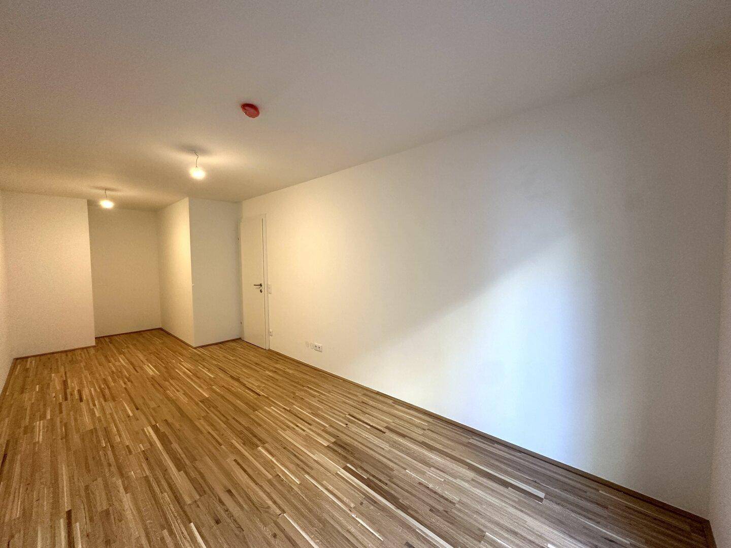 Eckzimmer mit Parkettboden und weißen Wänden, bietet viel Platz und Gestaltungsmöglichkeiten.