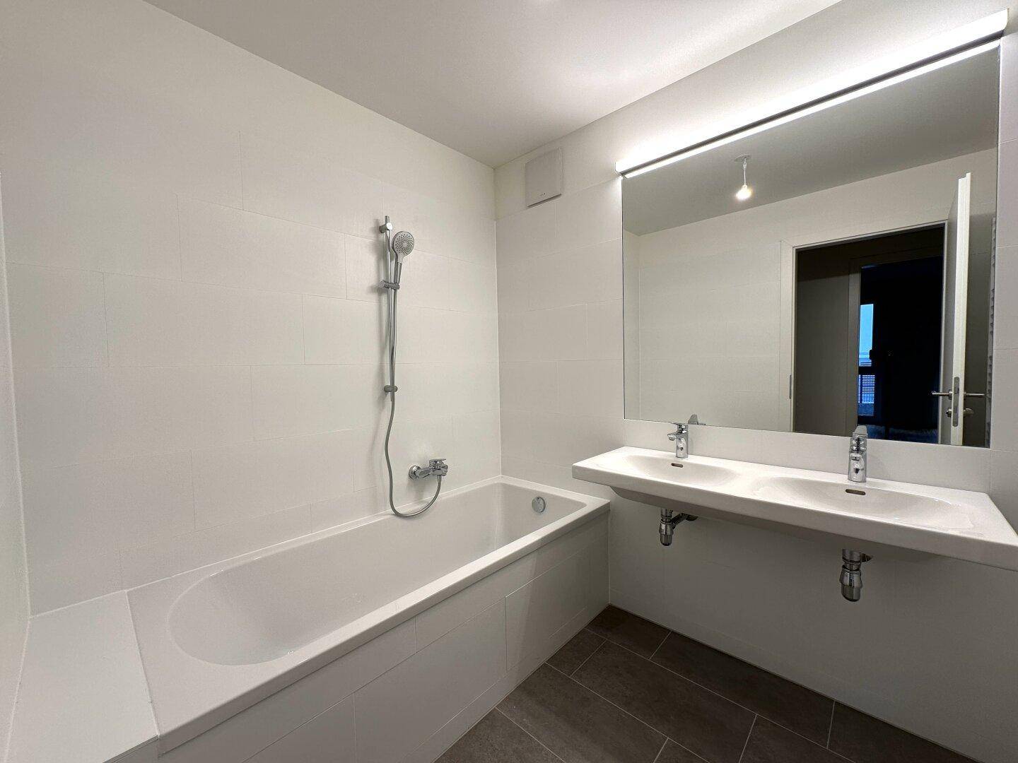Modernes Badezimmer mit Badewanne, Doppelwaschbecken und großem Spiegel, hell gefliest.