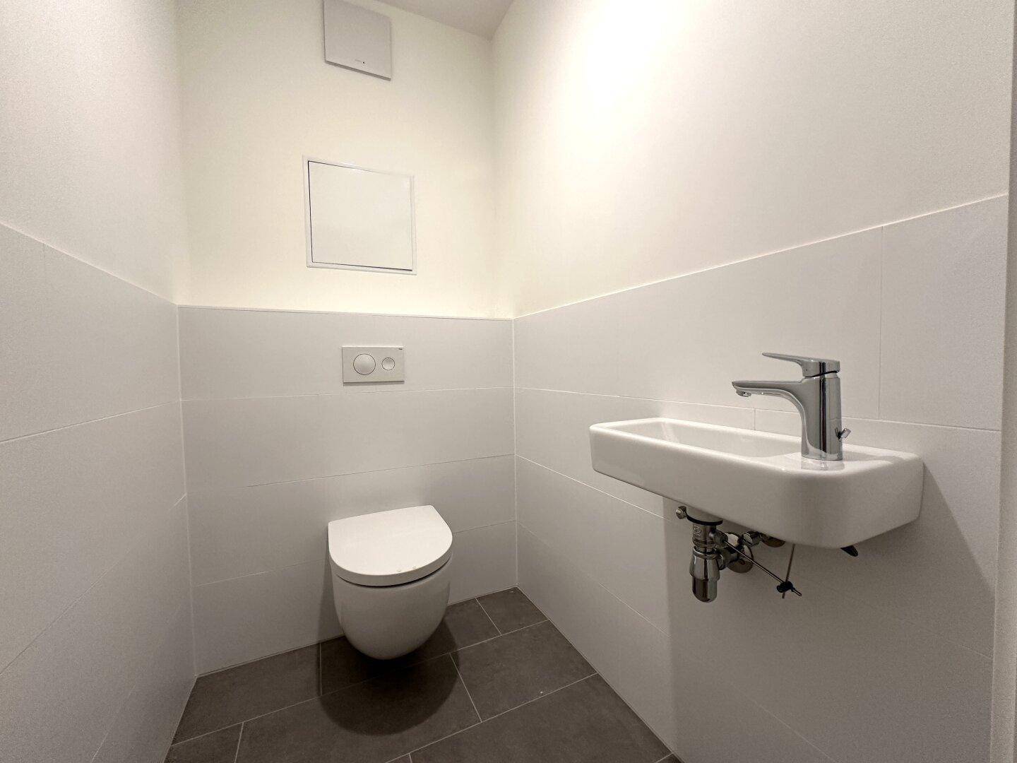 Separate Gästetoilette mit modernem Wand-WC und kleinem Handwaschbecken, in neutralen Farben gehalten.