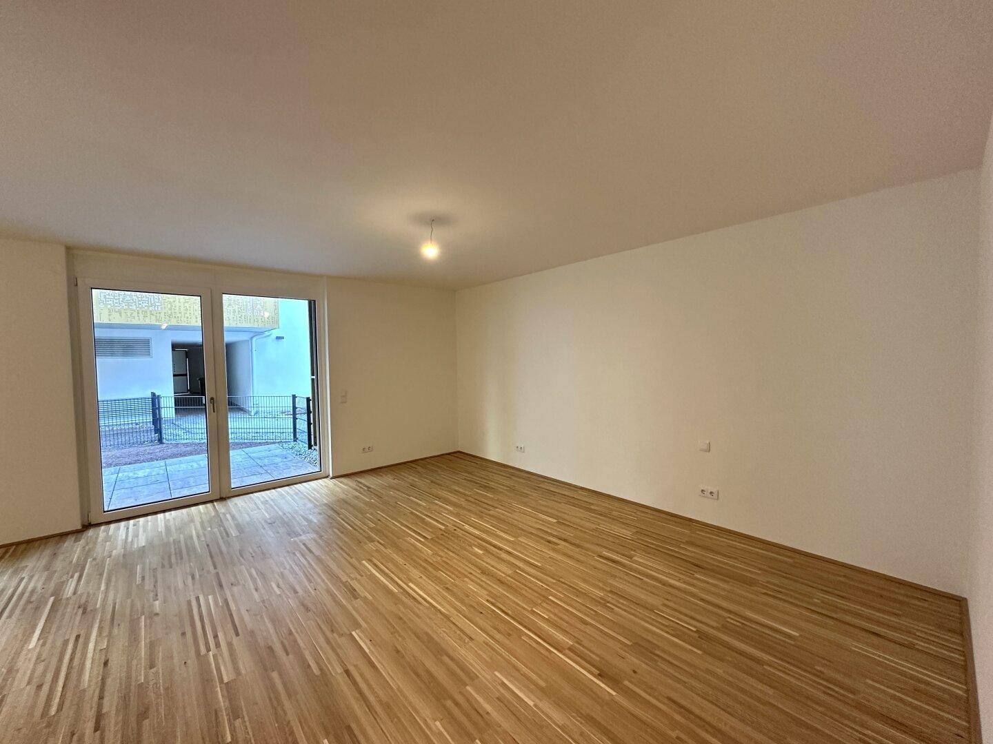 Geräumiges Wohnzimmer mit hellem Parkettboden und großen Glastüren, die Zugang zur Terrasse bieten.
