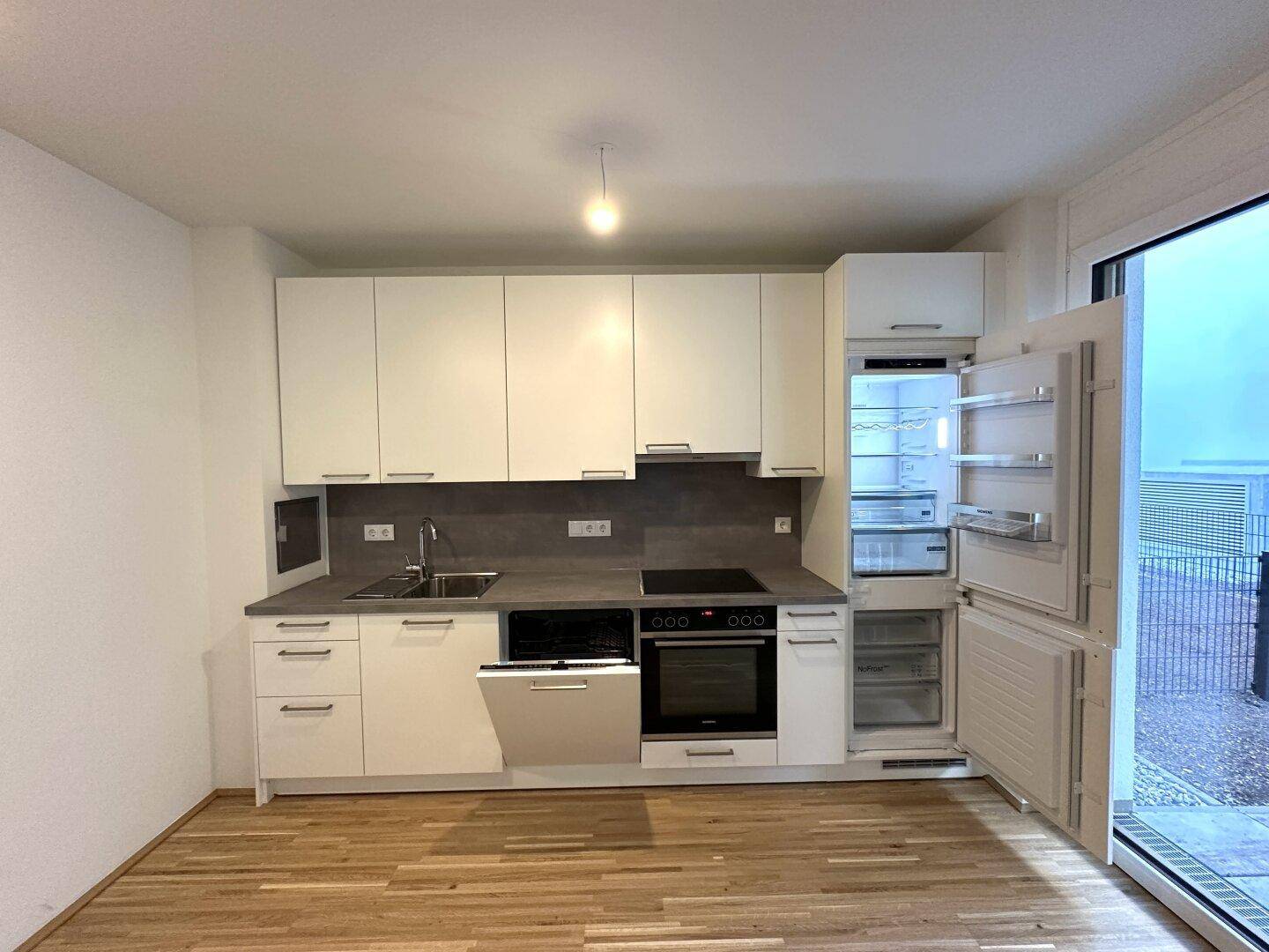 Voll ausgestattete, moderne Küche mit geöffnetem Kühlschrank und Geschirrspüler, bereit zur ersten Nutzung.