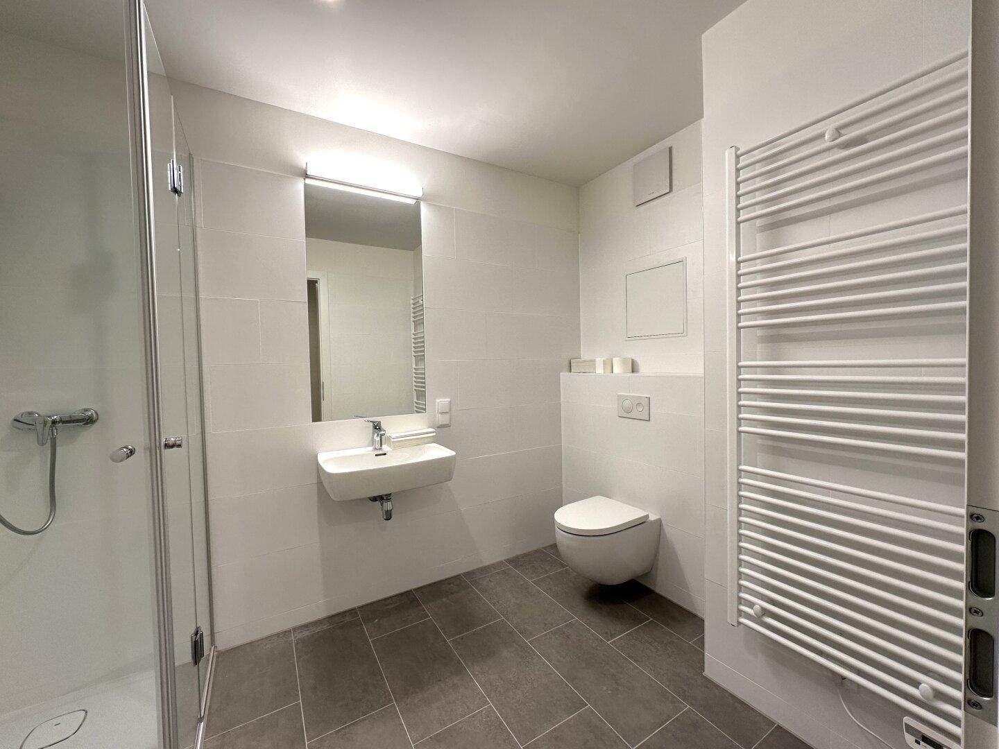 Modernes Badezimmer mit ebenerdiger Dusche, wandhängendem WC und beheiztem Handtuchhalter.