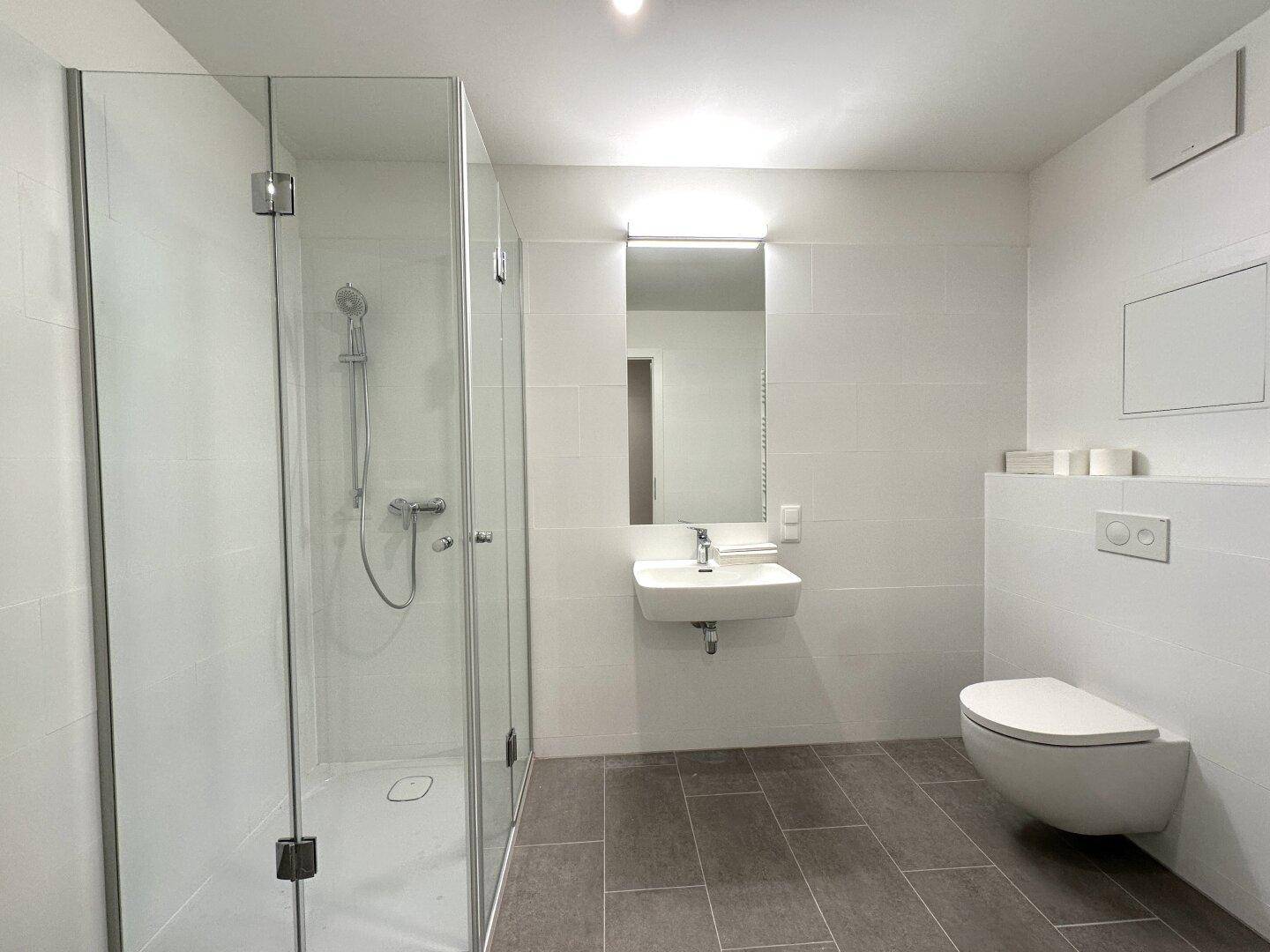 Helles Badezimmer mit großer, begehbarer Dusche, modernem Waschtisch und weißen Wandfliesen.