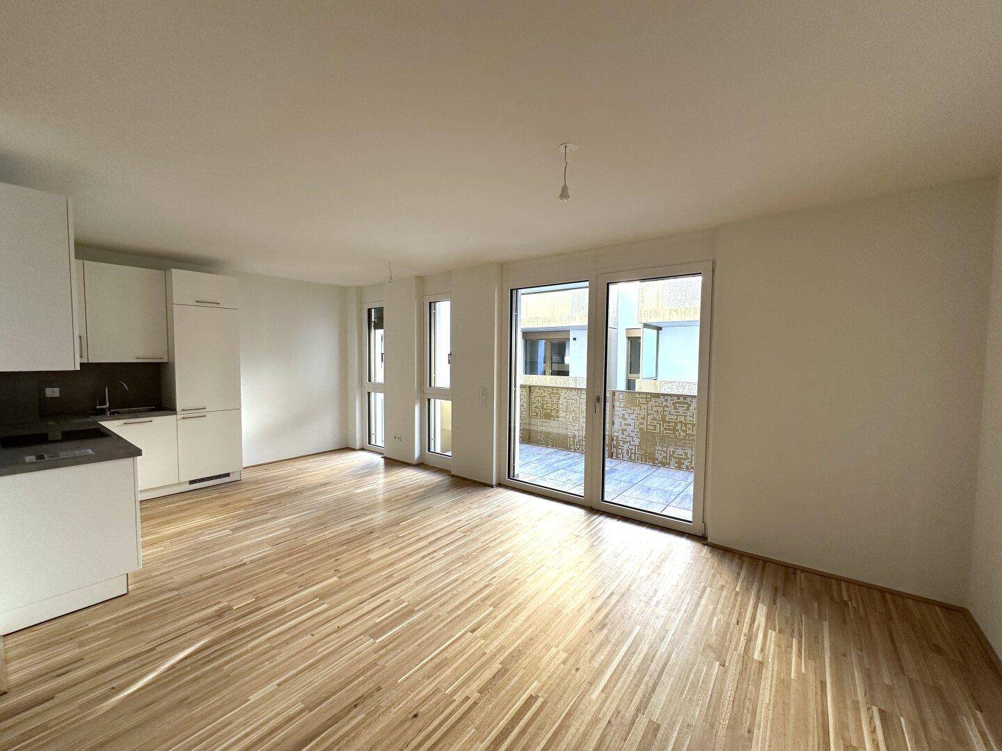 Lichtdurchfluteter Wohnbereich mit Zugang zum Balkon und großen Fenstern, die viel Tageslicht hereinlassen.
