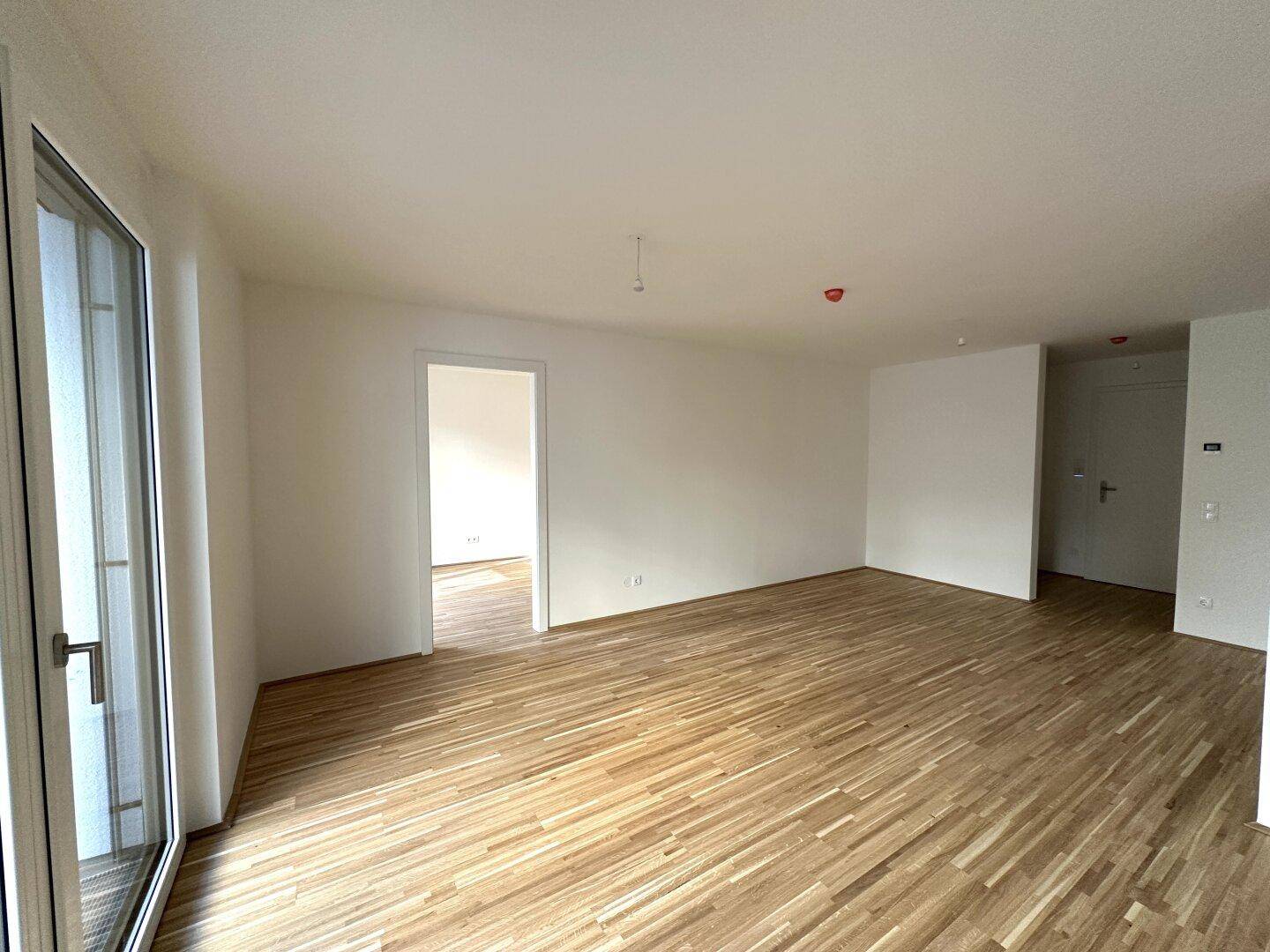 Geräumiger Wohnbereich mit hellem Parkettboden und offenem Zugang zu einem weiteren Zimmer, ideal für flexible Nutzung.