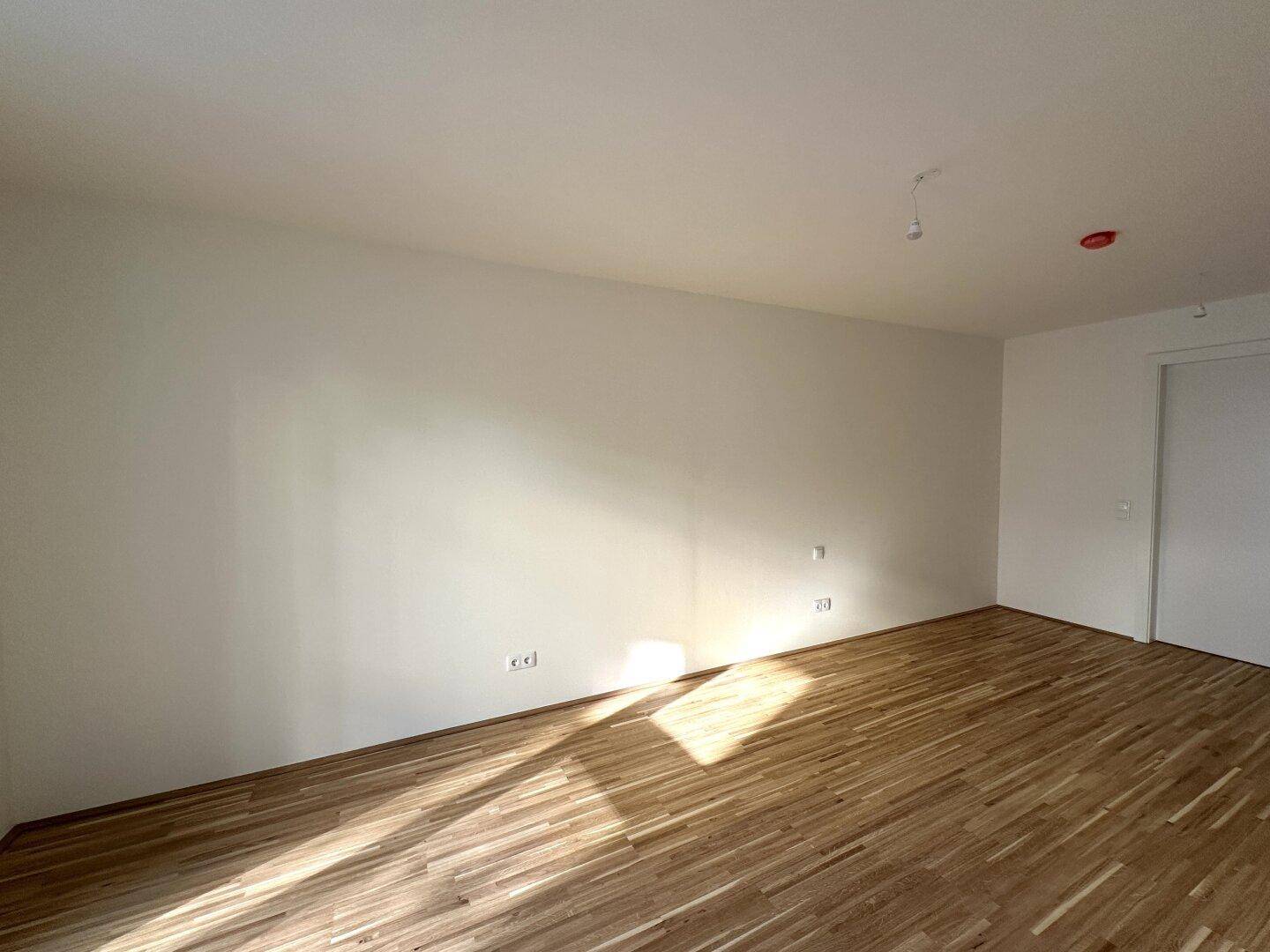 Helles, leeres Zimmer mit Parkettboden und weißen Wänden, bereit für individuelle Gestaltung und Nutzung.