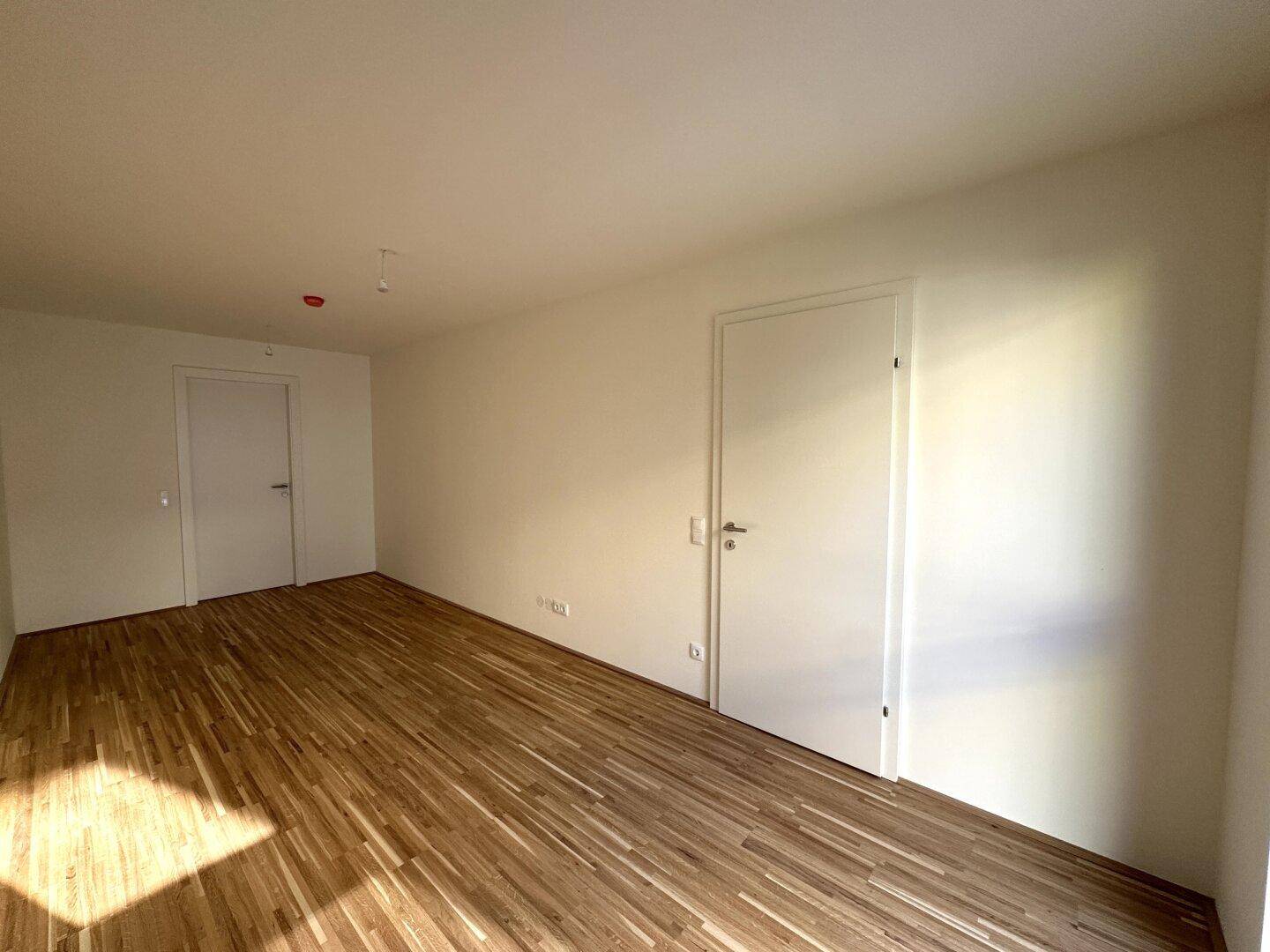Leeres Zimmer mit hellem Parkettboden und zwei weißen Türen, bietet vielseitige Einrichtungsmöglichkeiten.