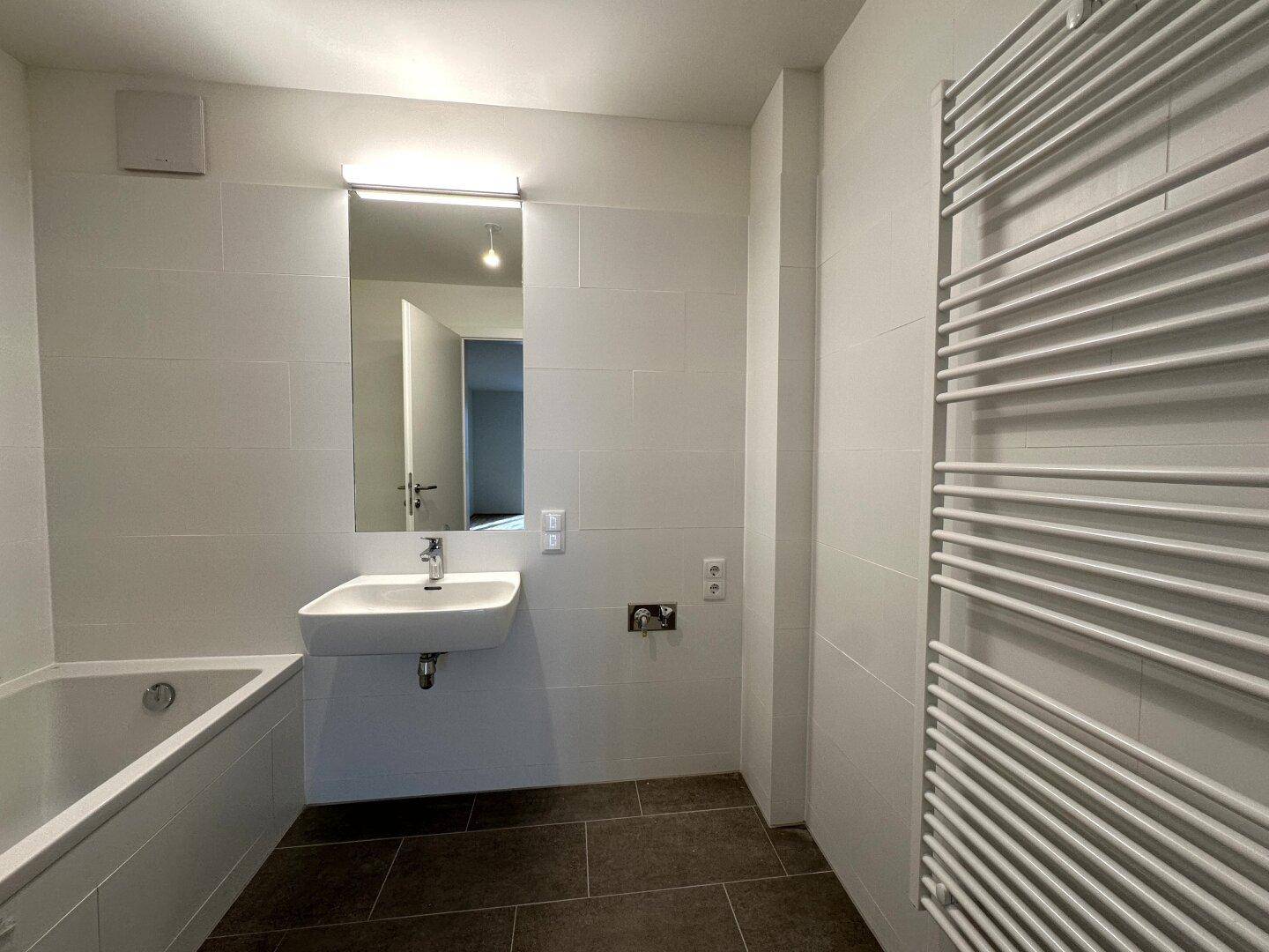 Modernes Badezimmer mit weißen Fliesen, Badewanne, Einzelwaschbecken und beheiztem Handtuchhalter.