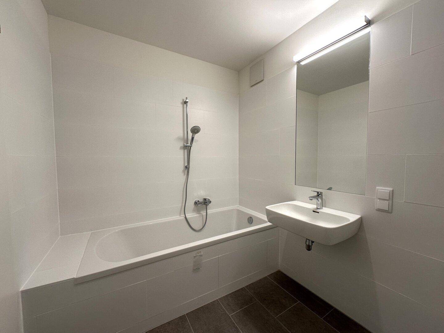 Helles Badezimmer mit Badewanne und integrierter Dusche, modern gefliest und mit Einzelwaschbecken ausgestattet.