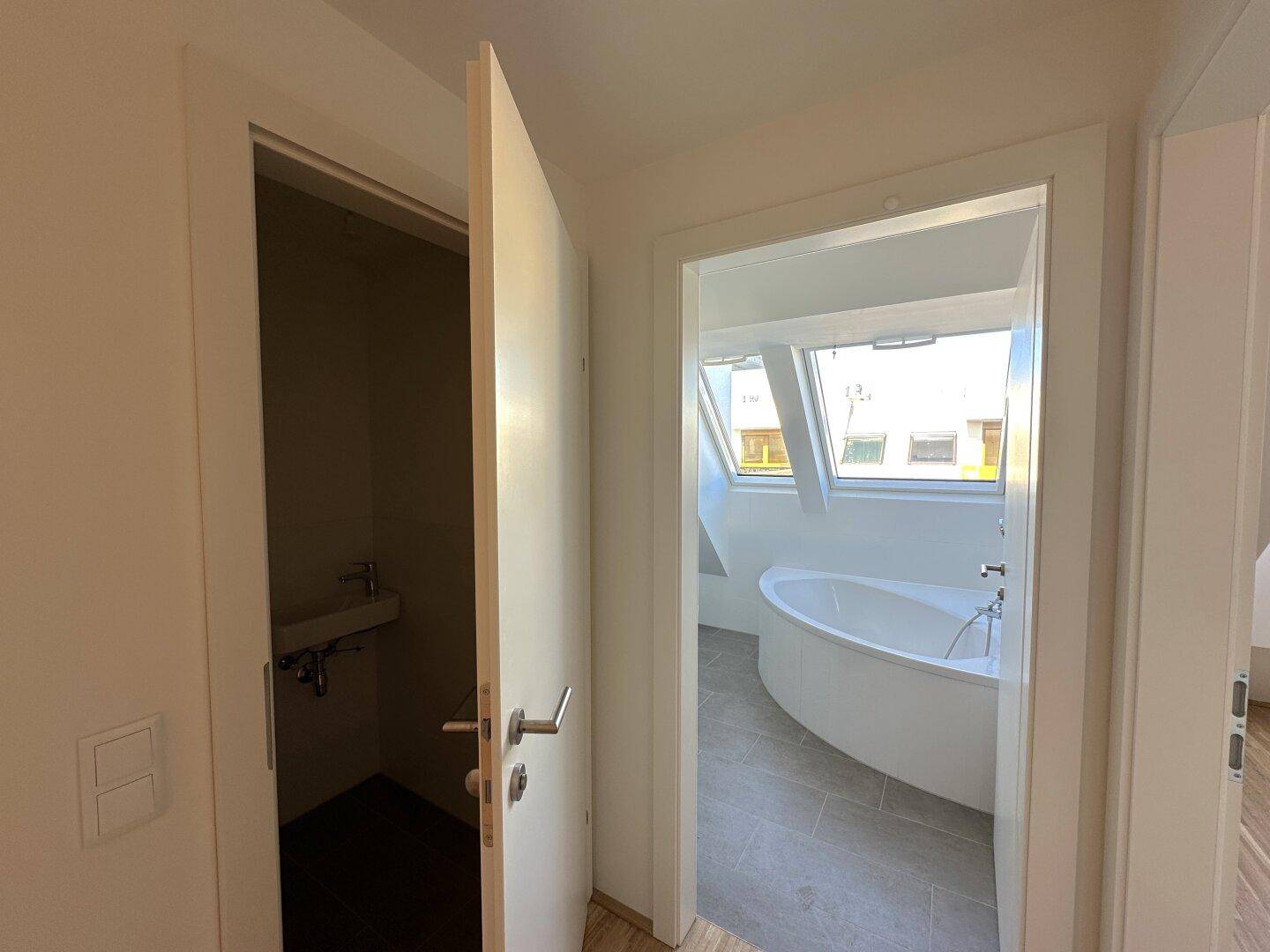 Eingangsbereich zu einem Badezimmer mit Badewanne und einem separaten Gäste-WC.
