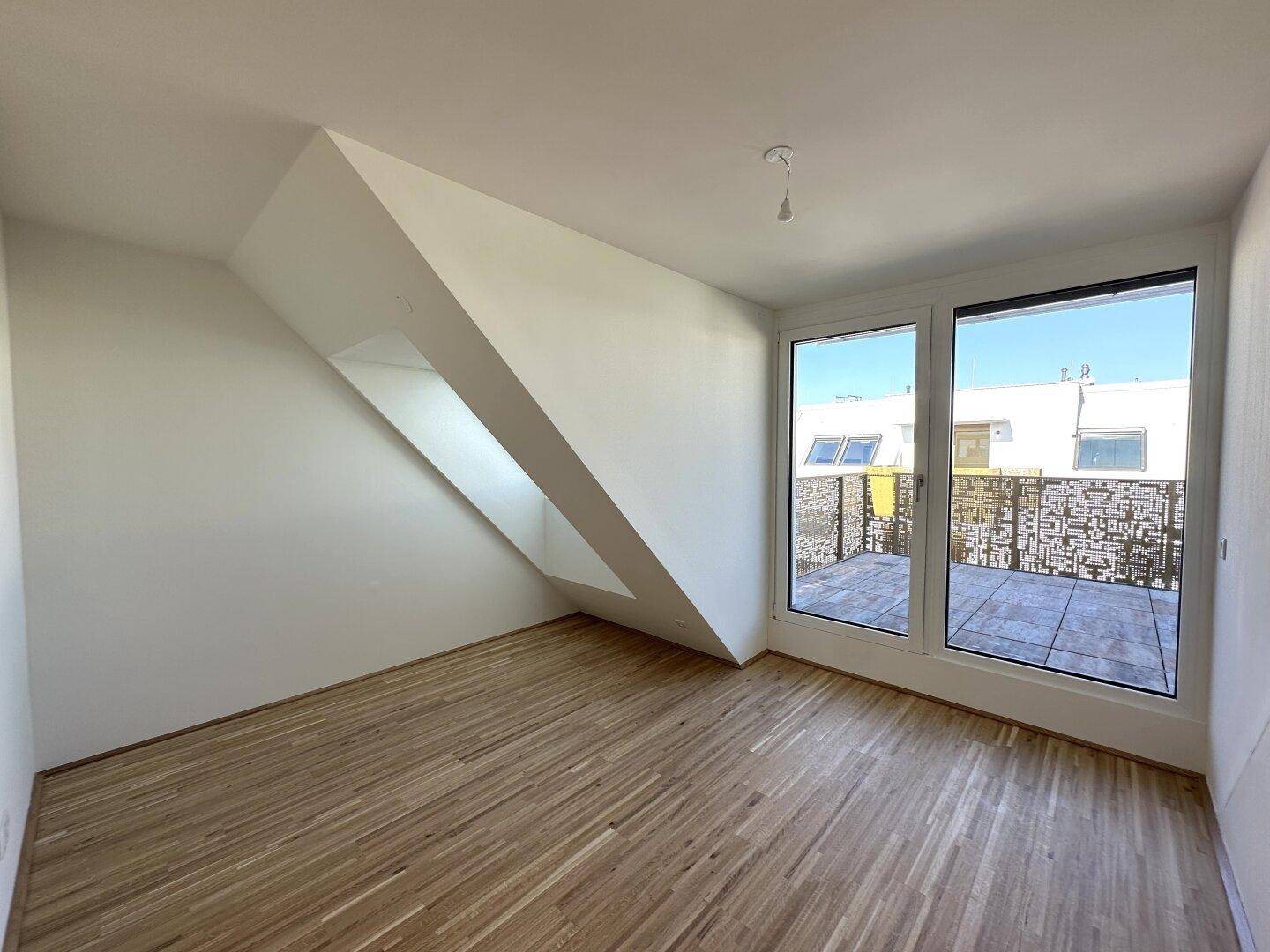 Helles Schlafzimmer mit Parkettboden, Dachschräge und großen Fenstern zur Terrasse.