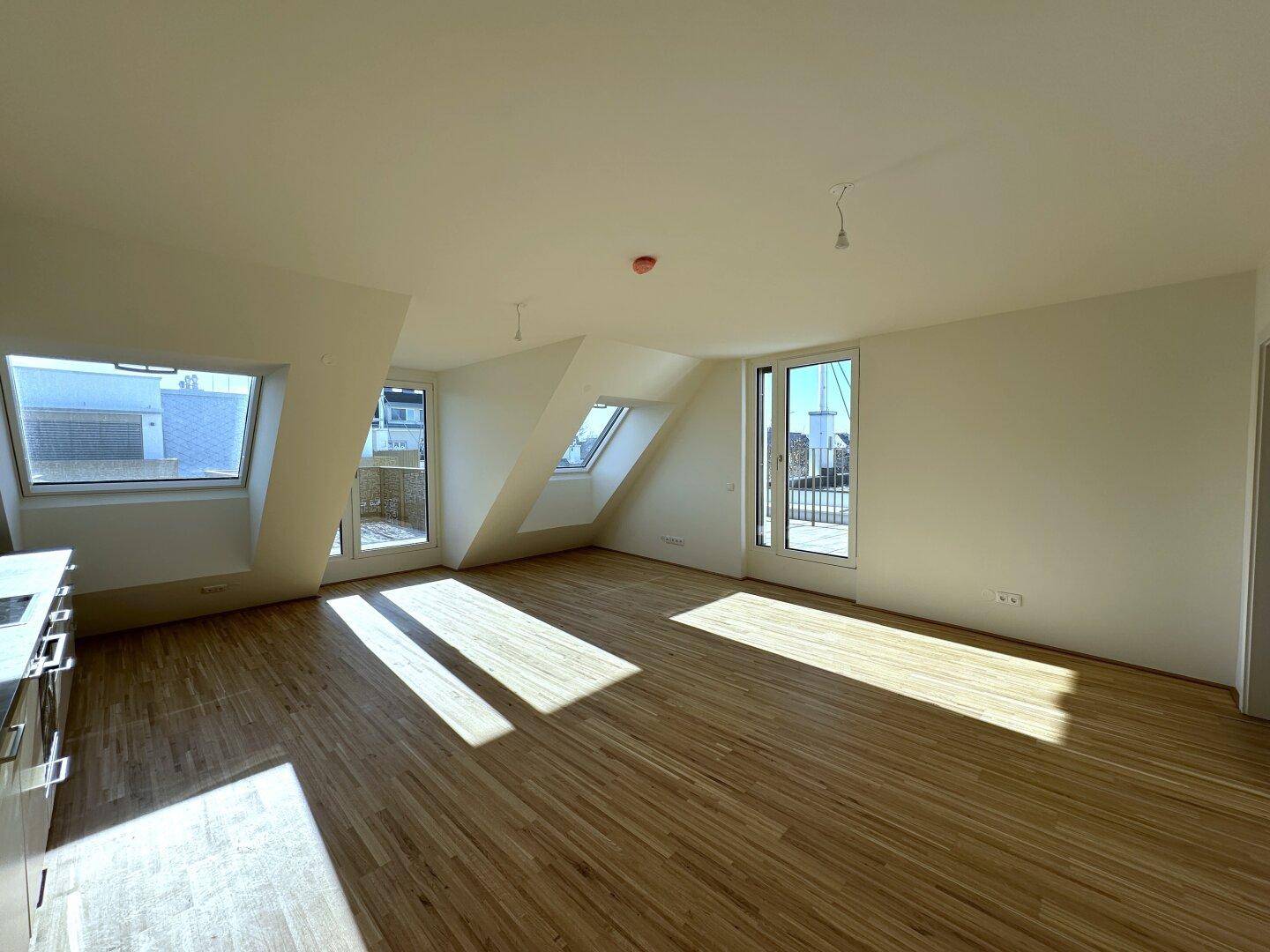 Geräumiger Wohnbereich mit viel Tageslicht, Parkettboden und direktem Zugang zur Dachterrasse.
