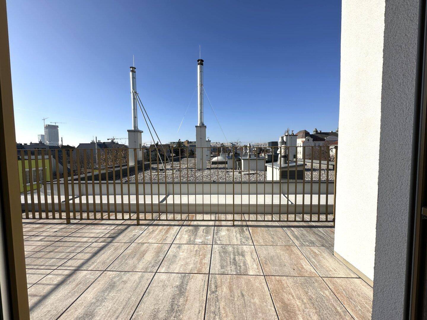 Weitläufige Dachterrasse mit Fliesenboden und Blick auf die Dächer der Stadt.