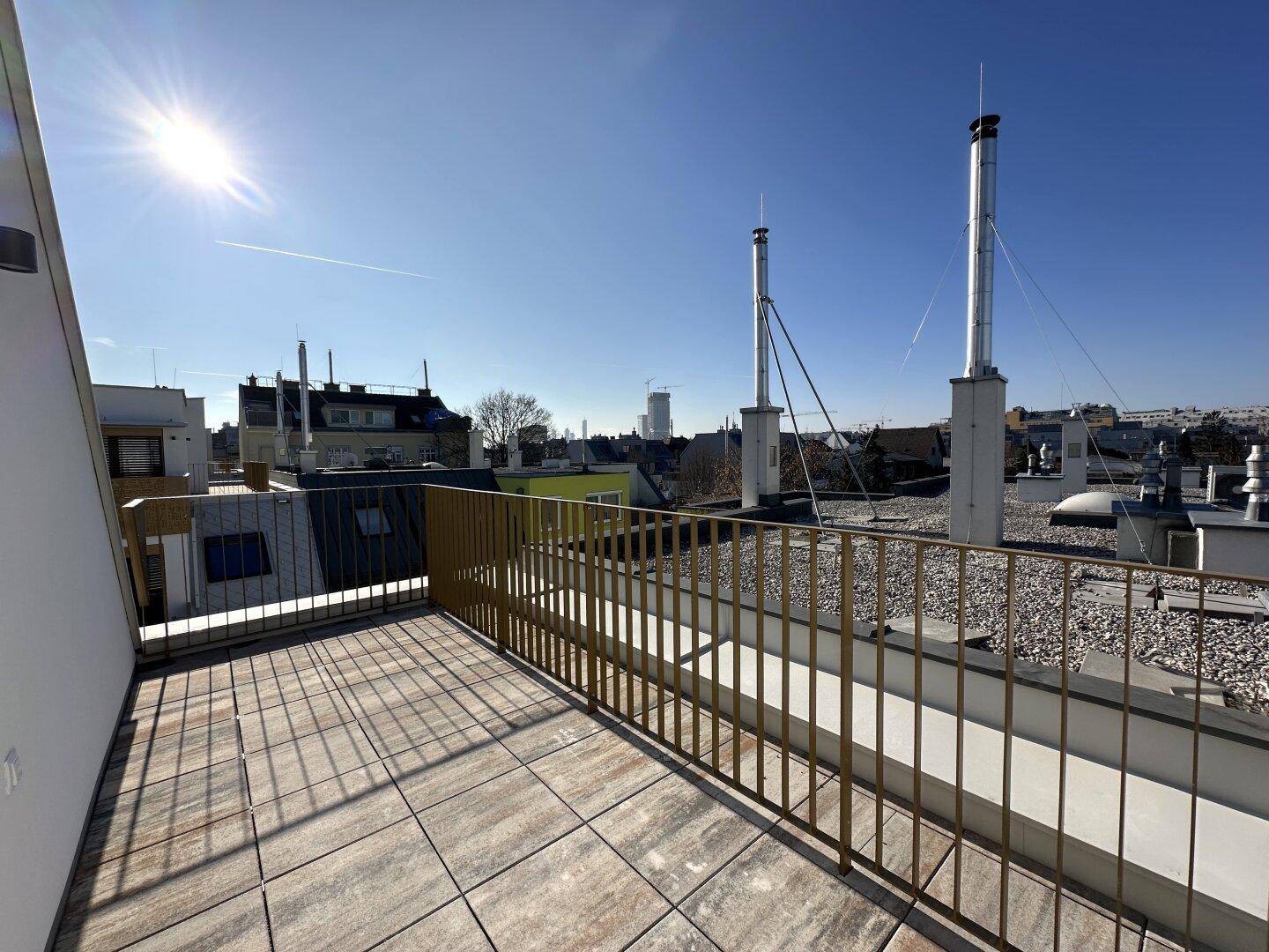 Sonnige Dachterrasse mit Fliesenboden und weitem Blick über die Stadt.