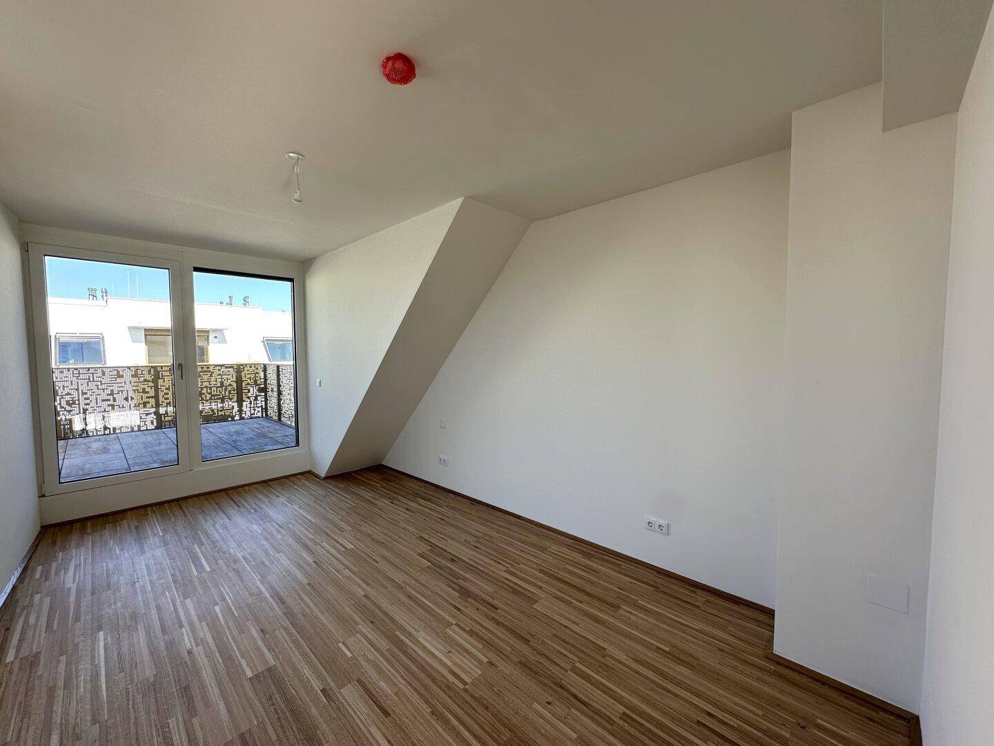 Helles Schlafzimmer mit Parkettboden, Dachschräge und Zugang zur Dachterrasse.