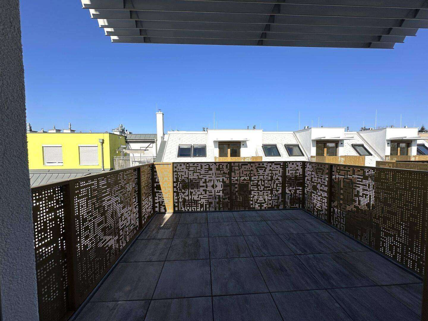 Große Dachterrasse mit modernen Fliesen und dekorativem Metallgeländer, bietet einen weiten Blick über die Dächer.