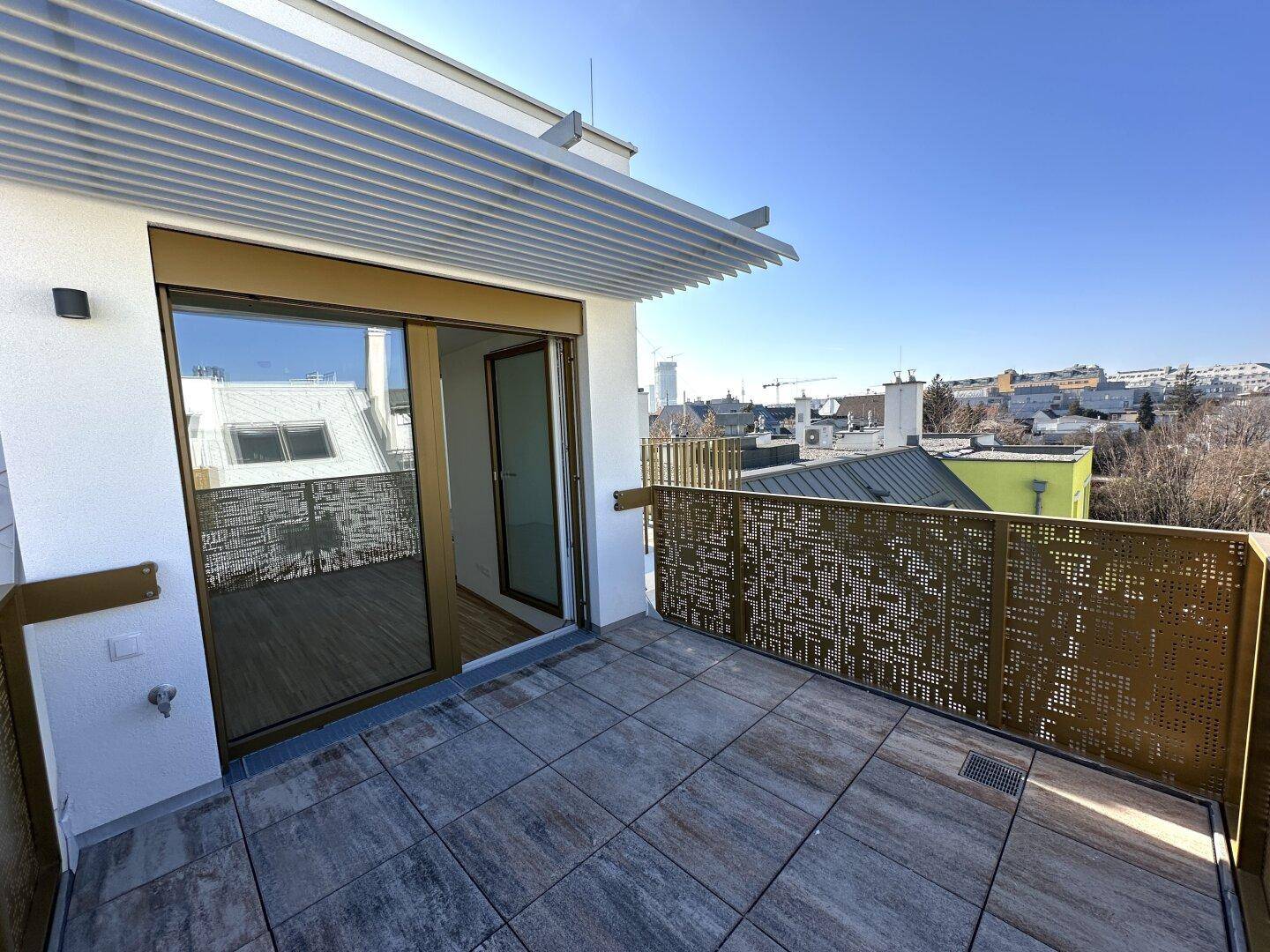 Sonnige Dachterrasse mit Zugang zum Innenbereich durch eine große Glasschiebetür und Blick über die Stadt.
