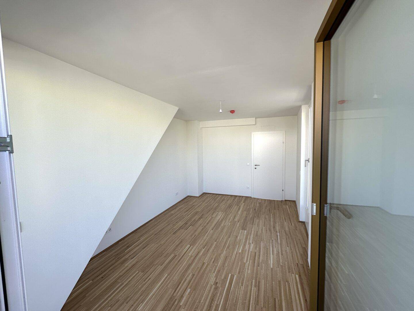 Helles, leeres Zimmer mit schrägen Wänden, Holzboden und viel Tageslicht, ideal als Schlafzimmer.