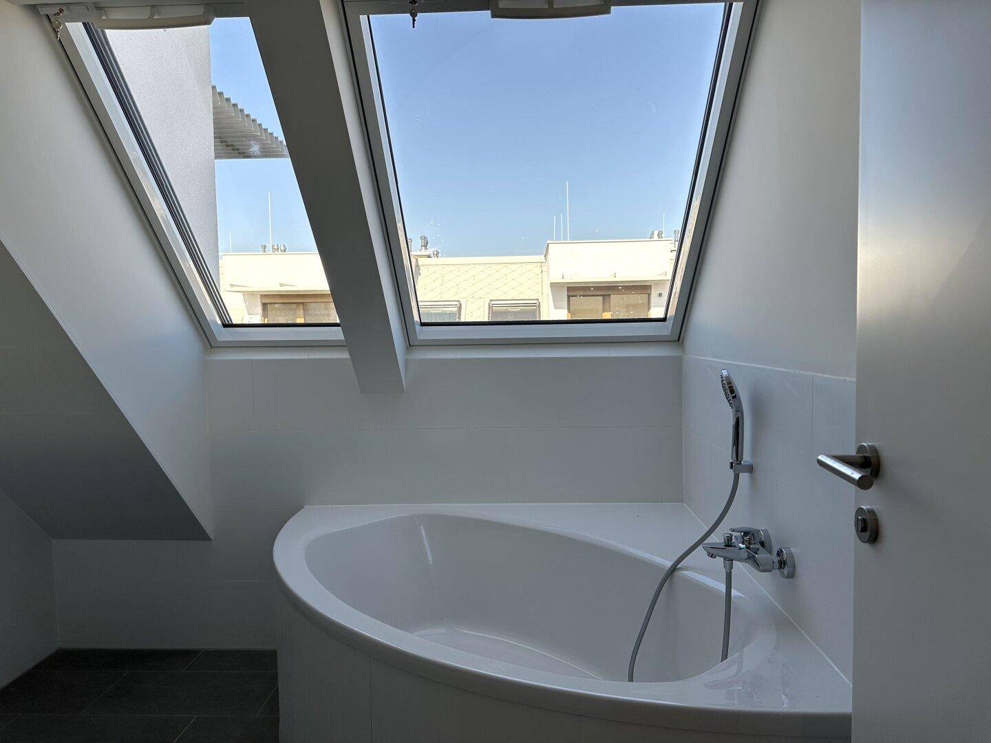 Eckbadewanne unter großen Dachfenstern, die viel natürliches Licht in das moderne Badezimmer bringen.