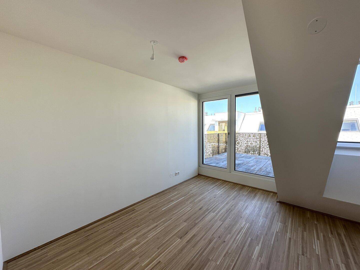 Geräumiges Zimmer mit Holzboden, Dachschrägen und Zugang zur sonnigen Terrasse.
