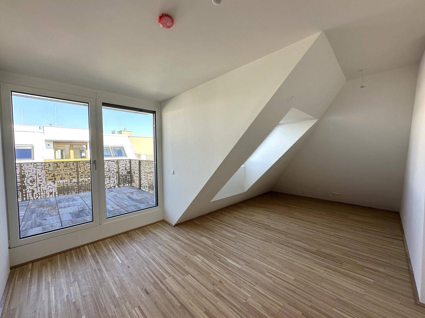 Helles Zimmer mit Holzboden, großen Fenstern und direktem Zugang zur Außenterrasse.
