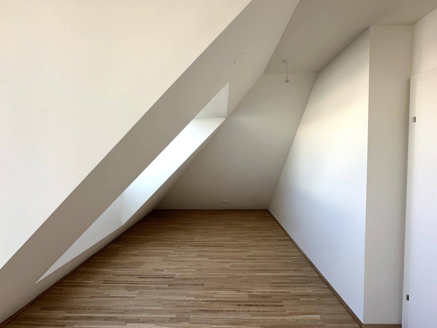 Helles Zimmer mit Holzboden und Dachschrägen, ideal als Schlaf- oder Arbeitszimmer.