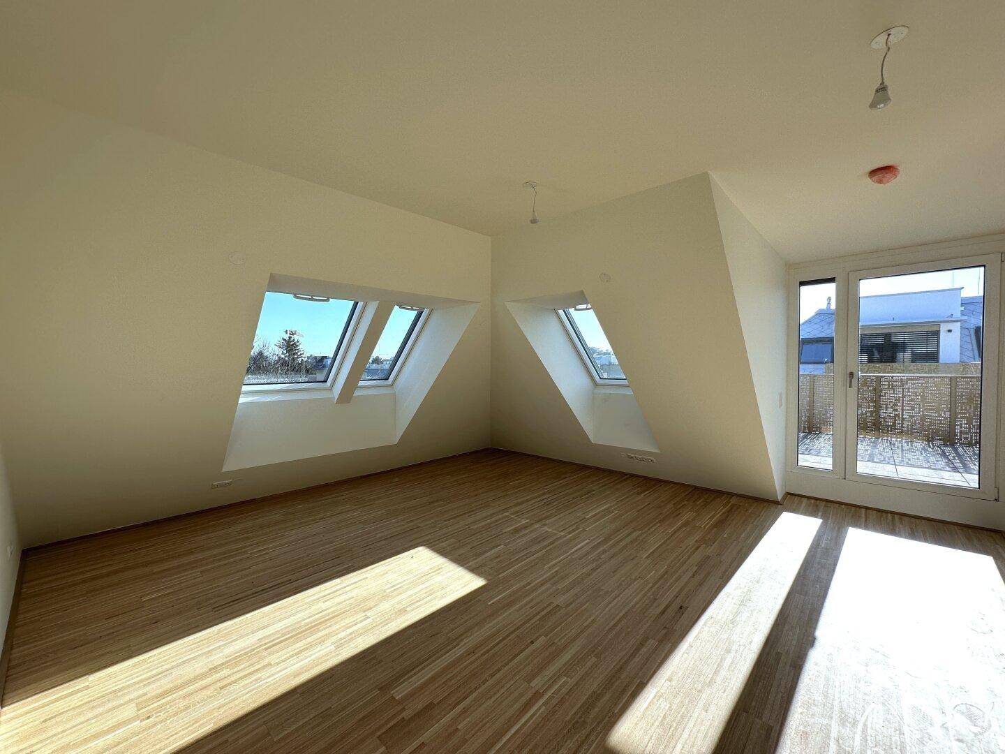 Lichtdurchfluteter Wohnbereich mit Holzboden, Dachfenstern und Zugang zur Terrasse.