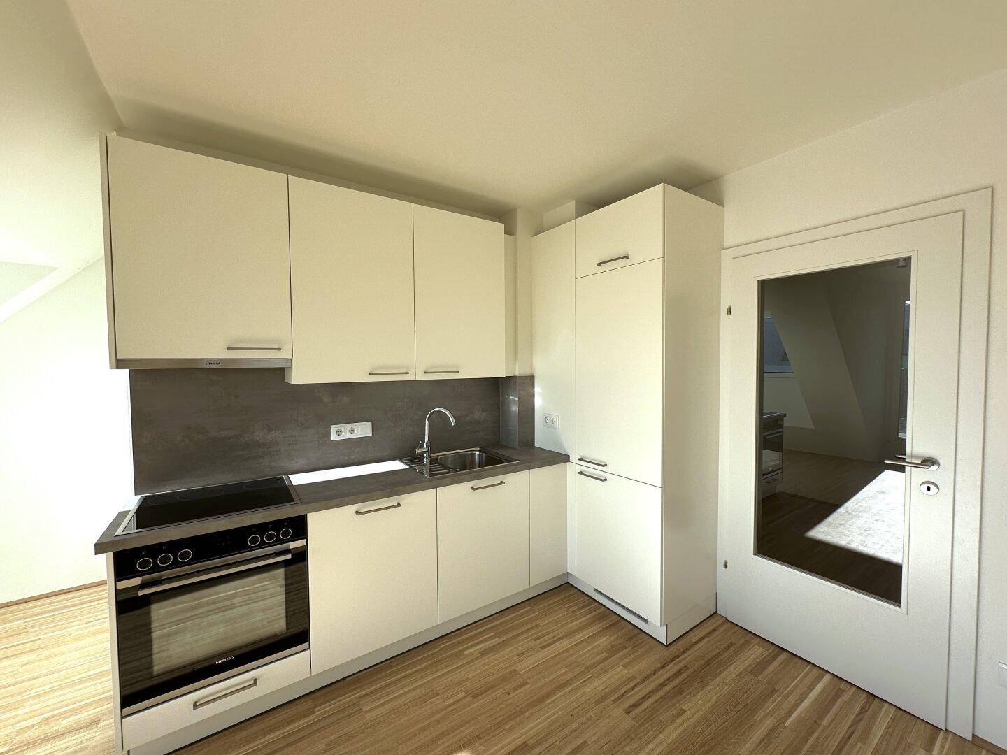 Moderne Einbauküche mit weißen Schränken, dunkler Arbeitsplatte und integrierten Geräten.