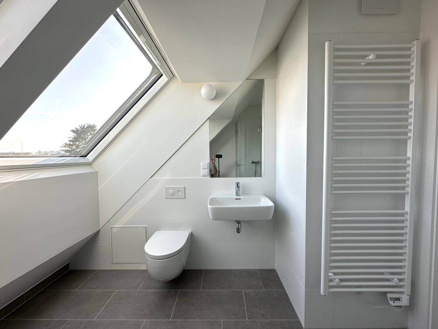 Modernes Badezimmer mit Waschtisch, Wand-WC, Handtuchheizkörper und Dachfenster.
