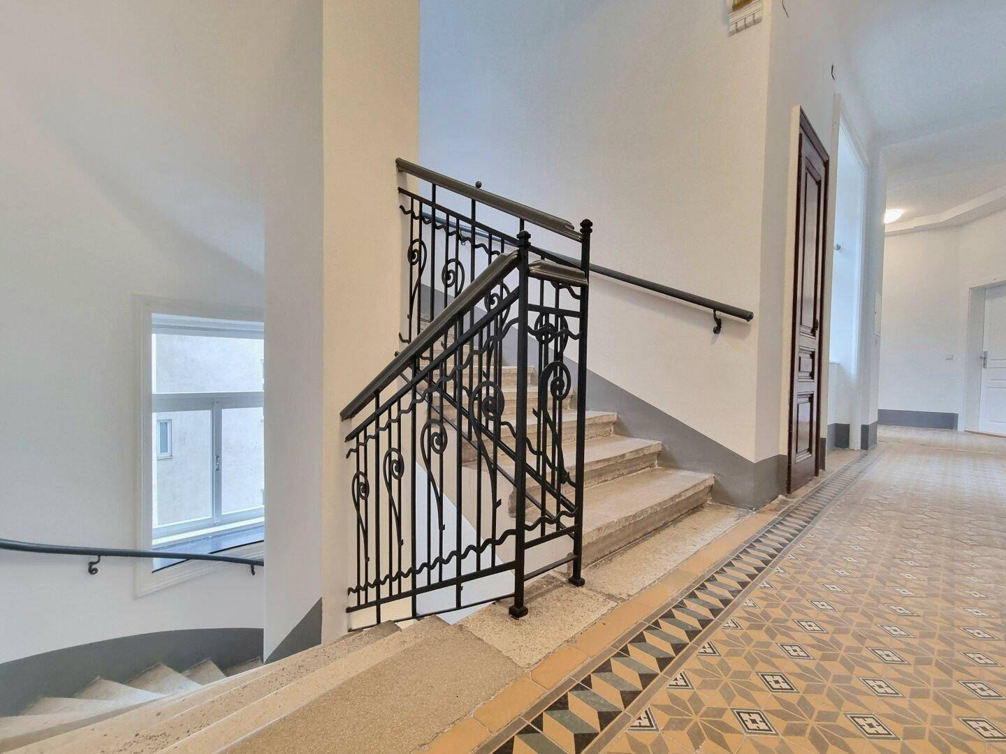 Treppenhaus mit kunstvollem Fliesenboden, schmiedeeisernem Geländer und natürlichem Lichteinfall.