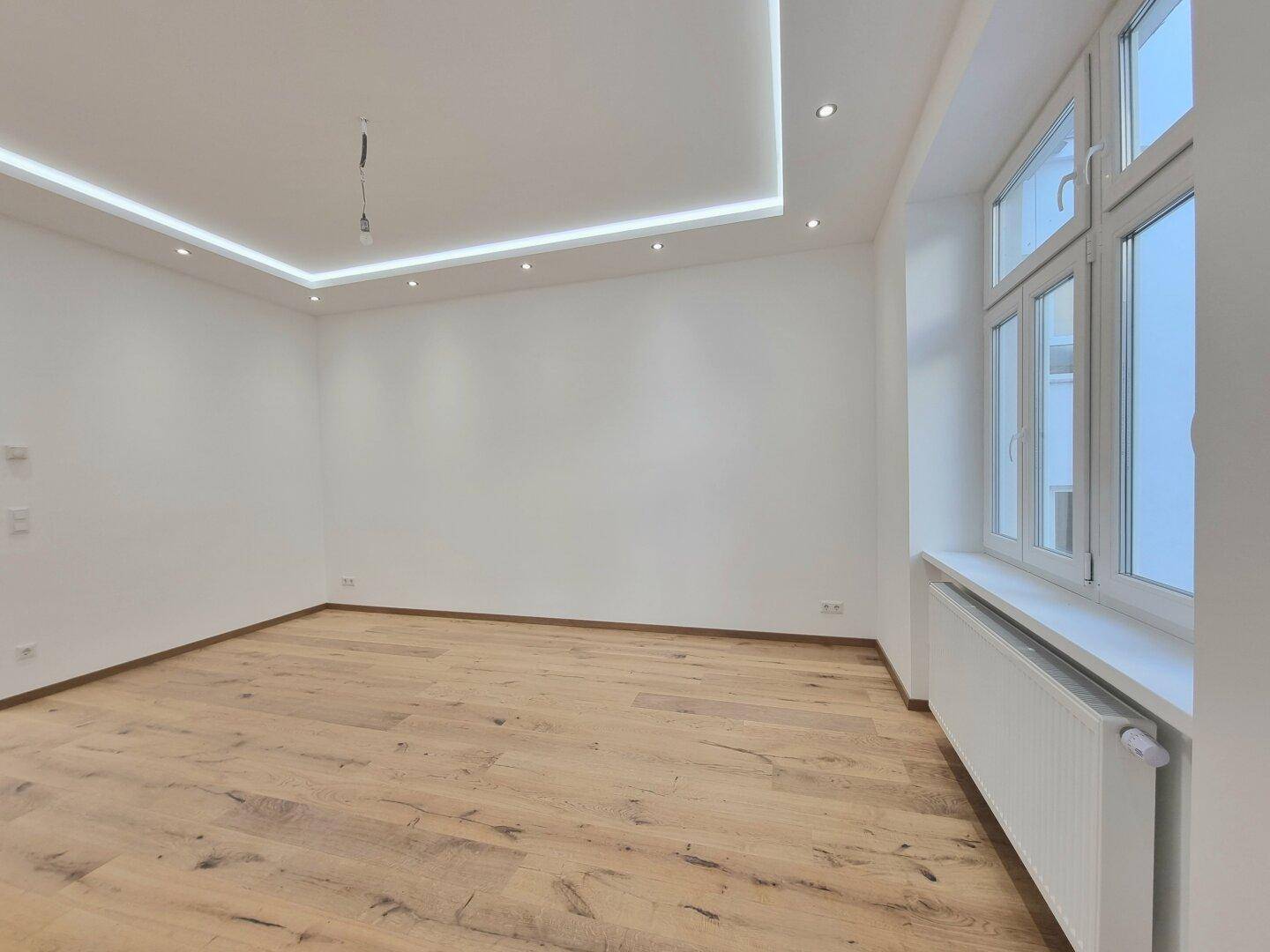 Modernes Zimmer mit Eichenparkett und integrierter Deckenbeleuchtung, das durch ein großes Fenster viel Licht erhält.