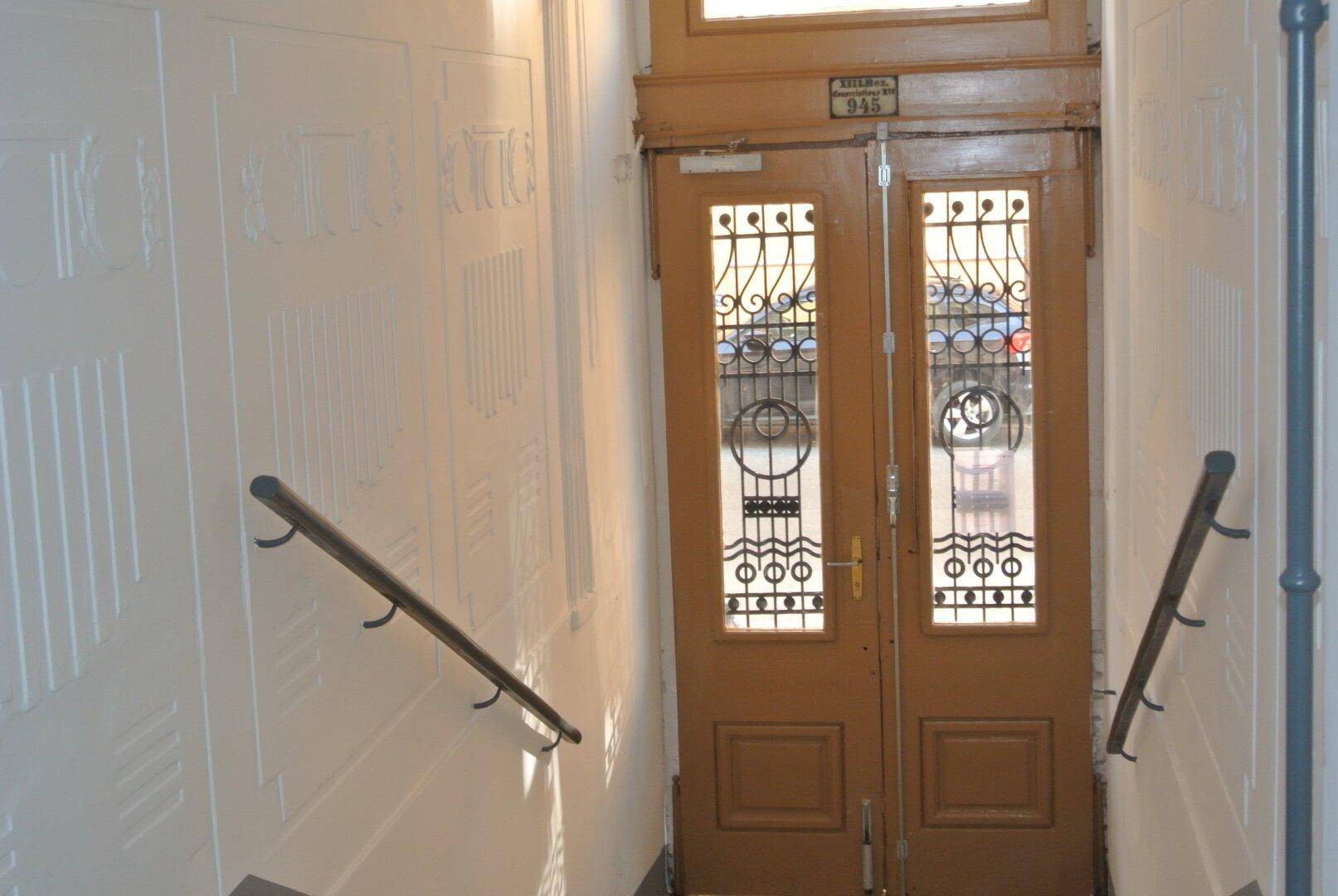 Detailansicht einer verzierten Holztür mit kunstvollen Glaspaneelen im Treppenhaus.