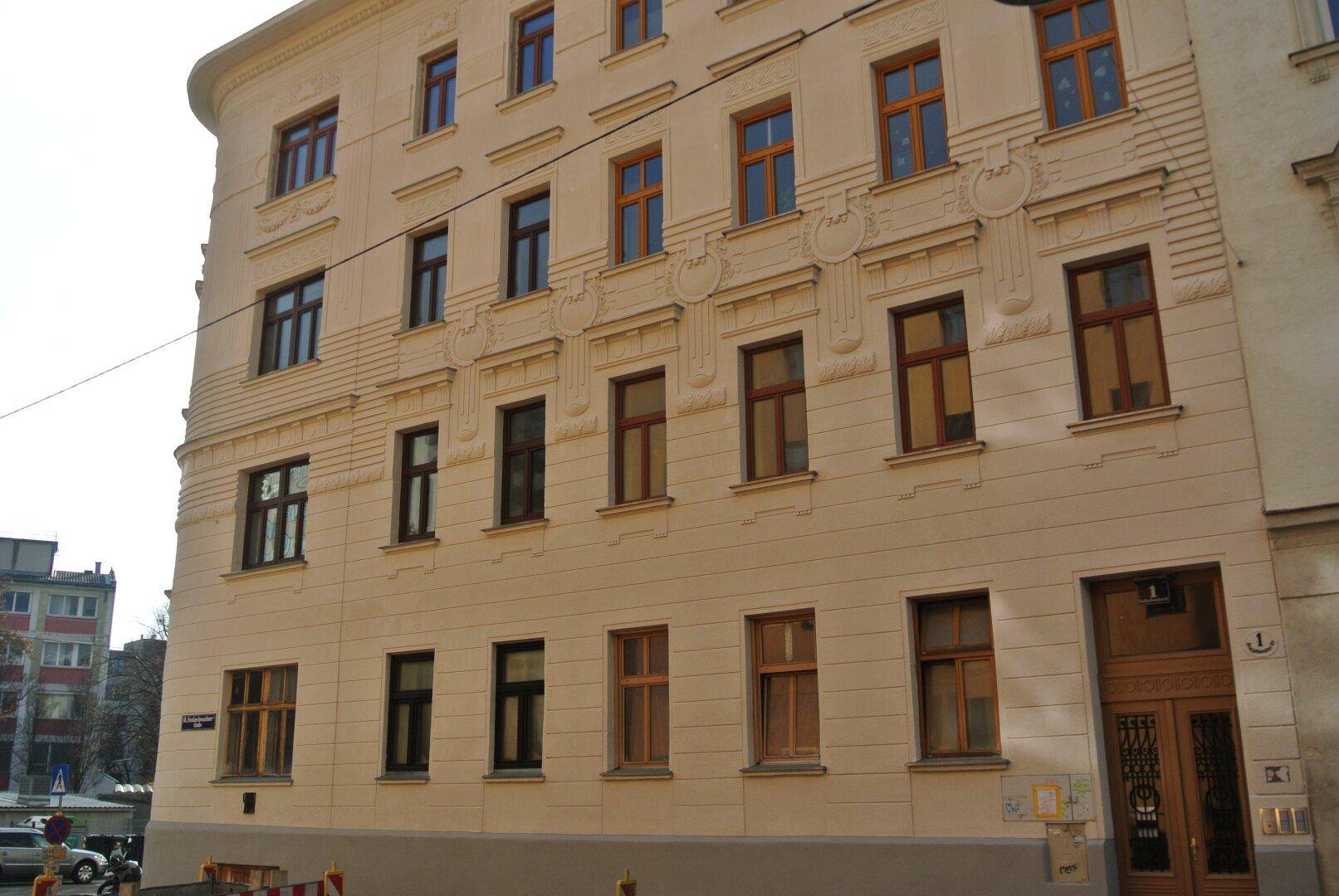 Detailansicht der historischen Fassade mit verzierten Fenstern und dem Haupteingang des Gebäudes.