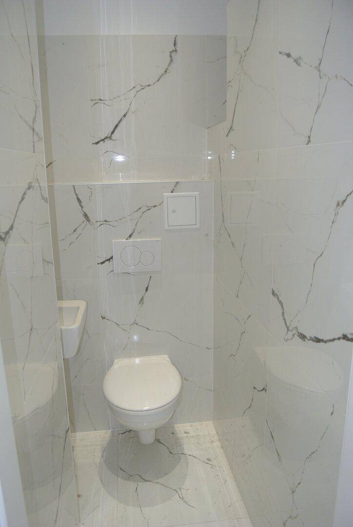 Kleines Gäste-WC mit modernen Marmoroptik-Fliesen, wandhängendem WC und kompaktem Waschbecken.