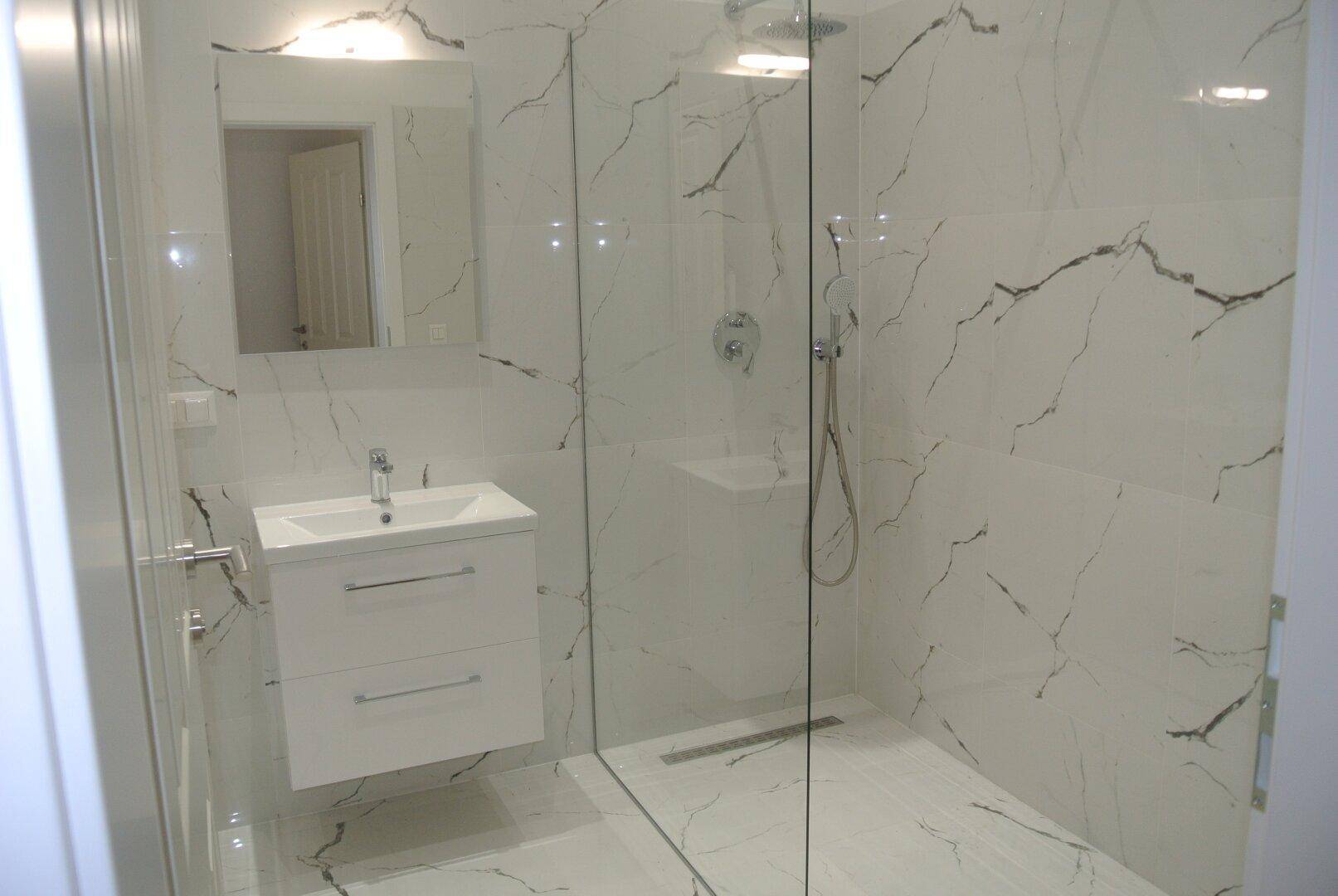 Modernes Badezimmer mit Marmoroptik-Fliesen, schwebendem Waschtisch und großer begehbarer Dusche.