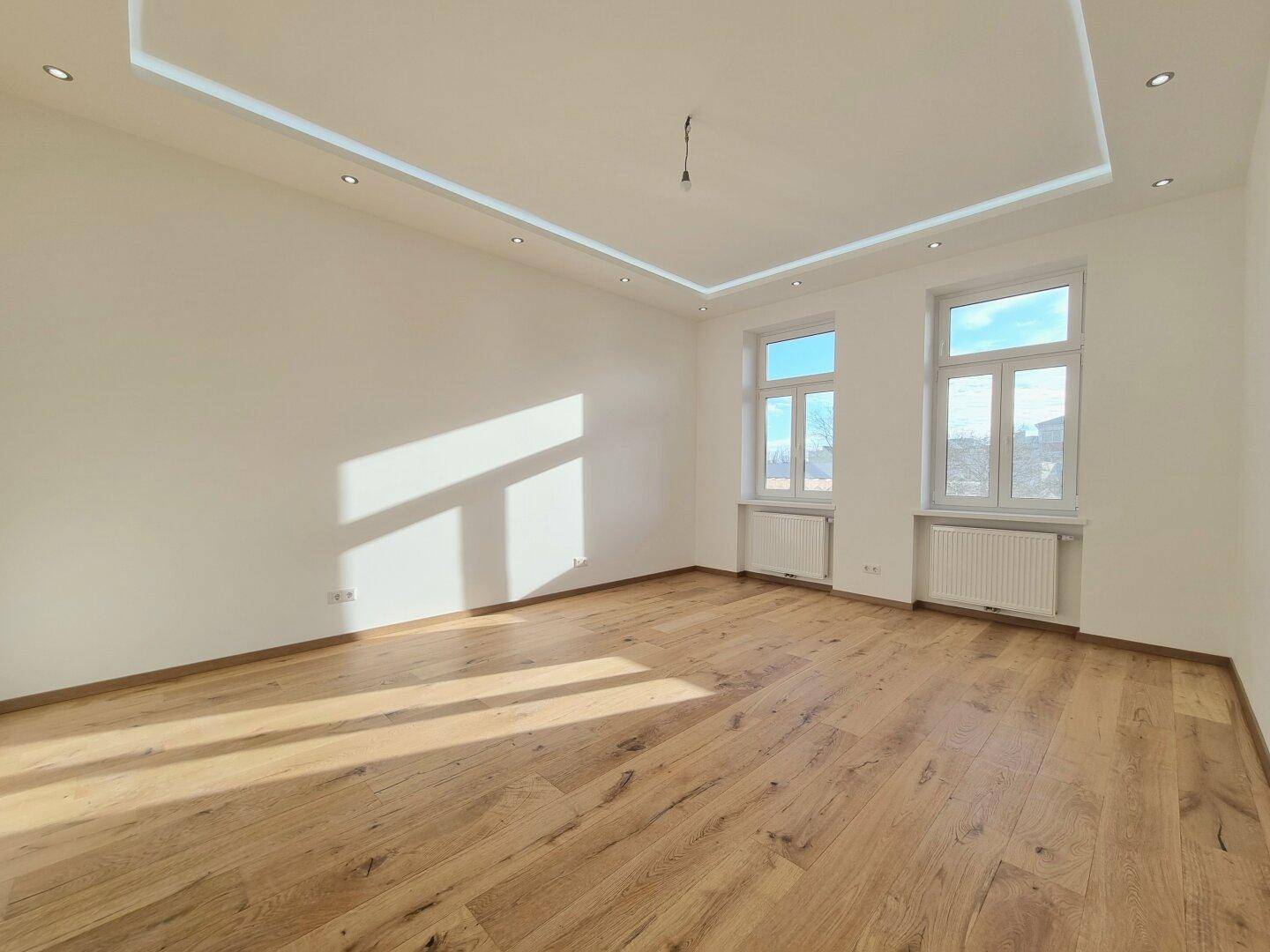 Geräumiges, helles Zimmer mit neuem Parkettboden, weißen Wänden und moderner Deckenbeleuchtung.