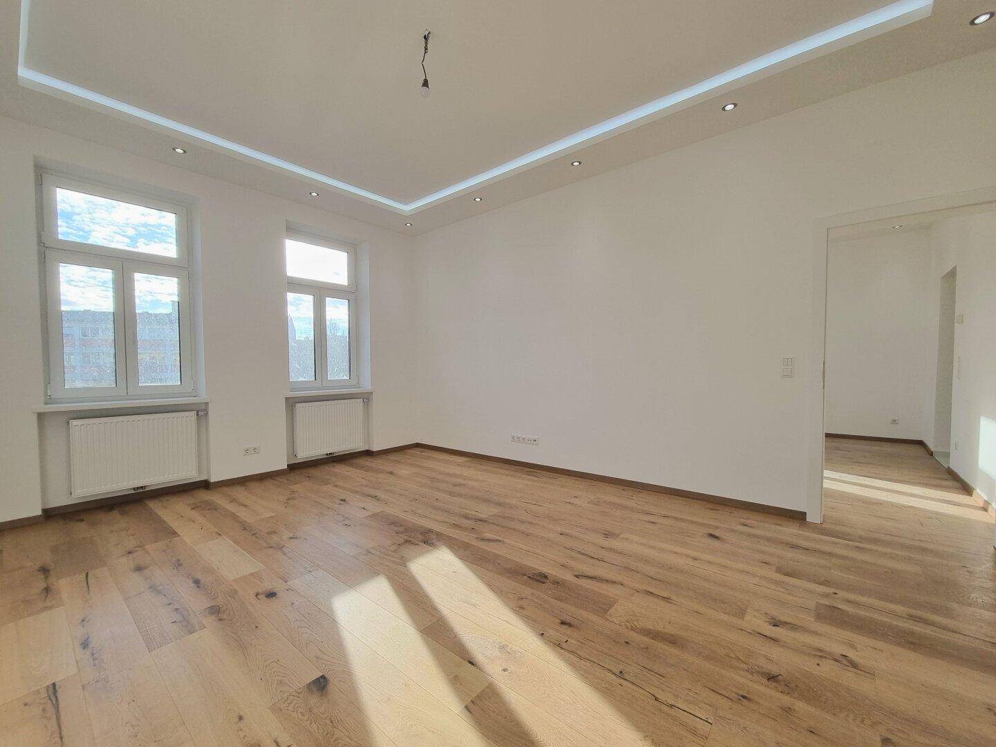 Lichtdurchflutetes Zimmer mit hellem Parkettboden, weißen Wänden und eleganter Deckenbeleuchtung.