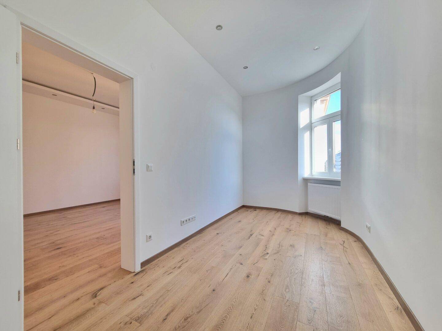 Heller Raum mit Holzboden, weißen Wänden und einem eleganten Erkerfenster.