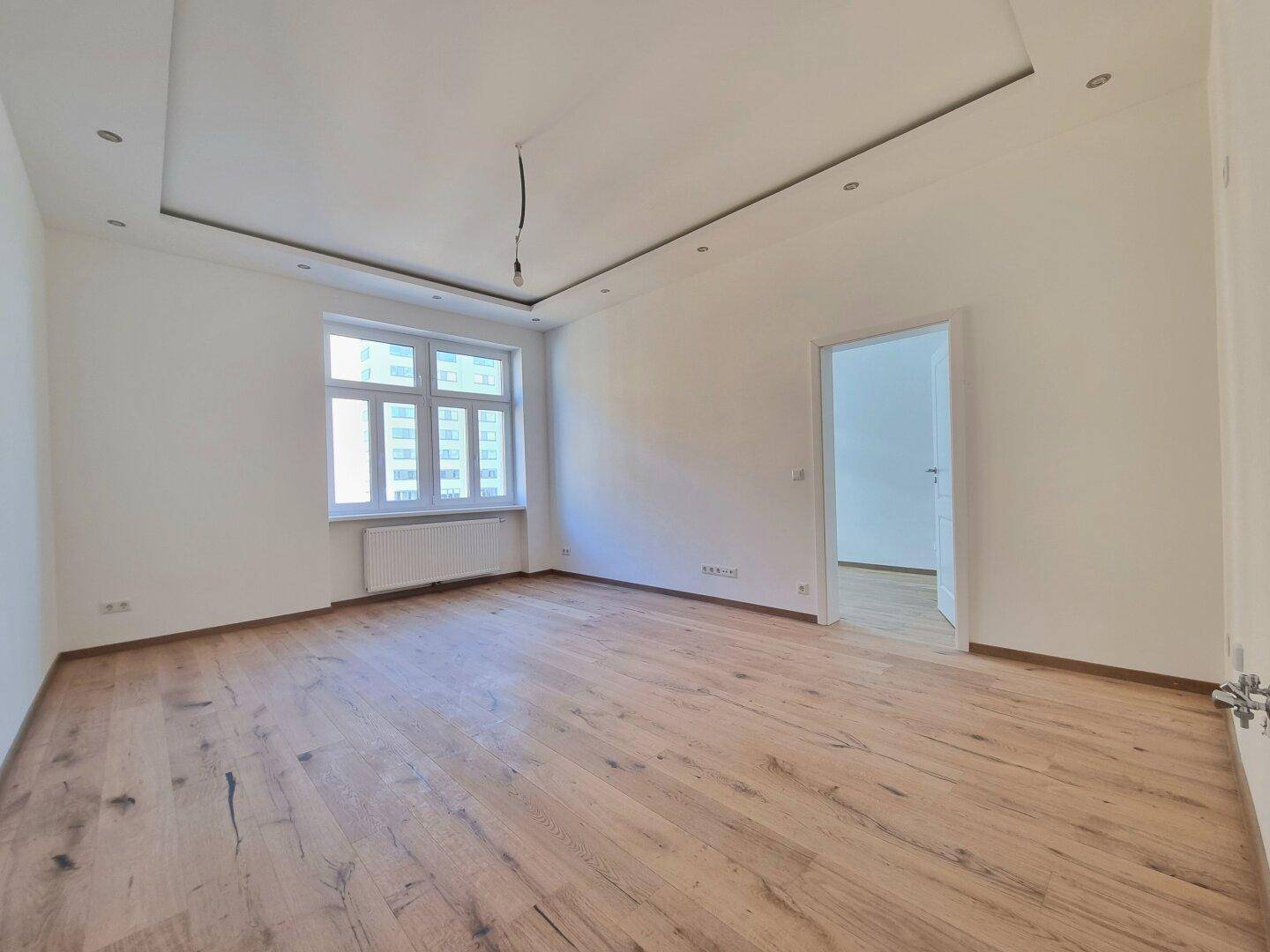 Geräumiger, heller Raum mit Holzboden, weißen Wänden und einem großen Fenster.
