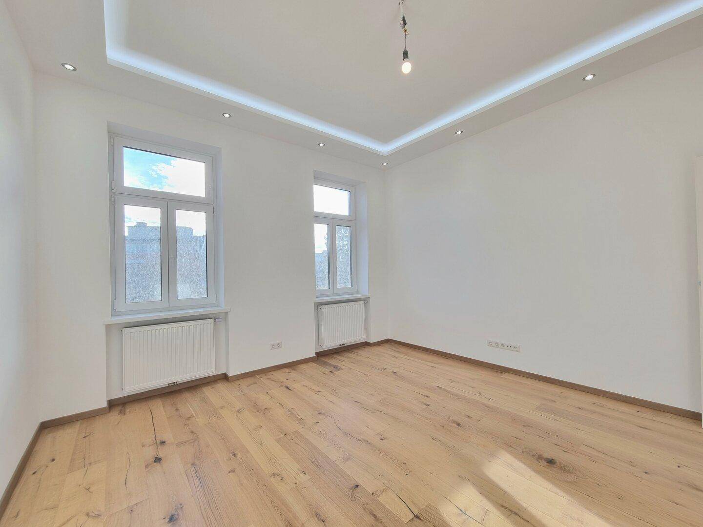Helles und geräumiges Zimmer mit modernem Holzboden und zwei großen Fenstern.