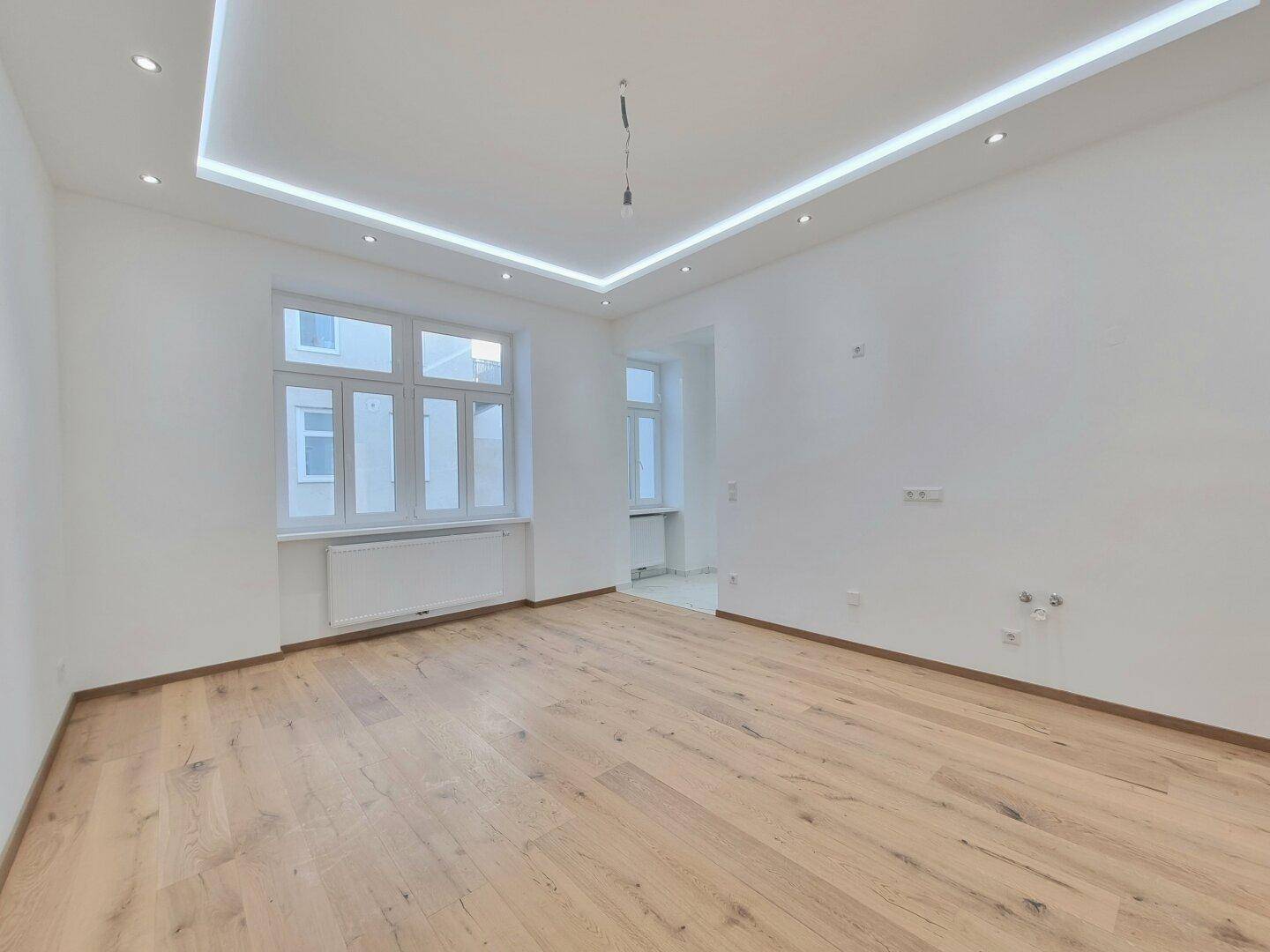Großes Zimmer mit Holzboden, weißen Wänden und mehreren Fenstern für viel Tageslicht.