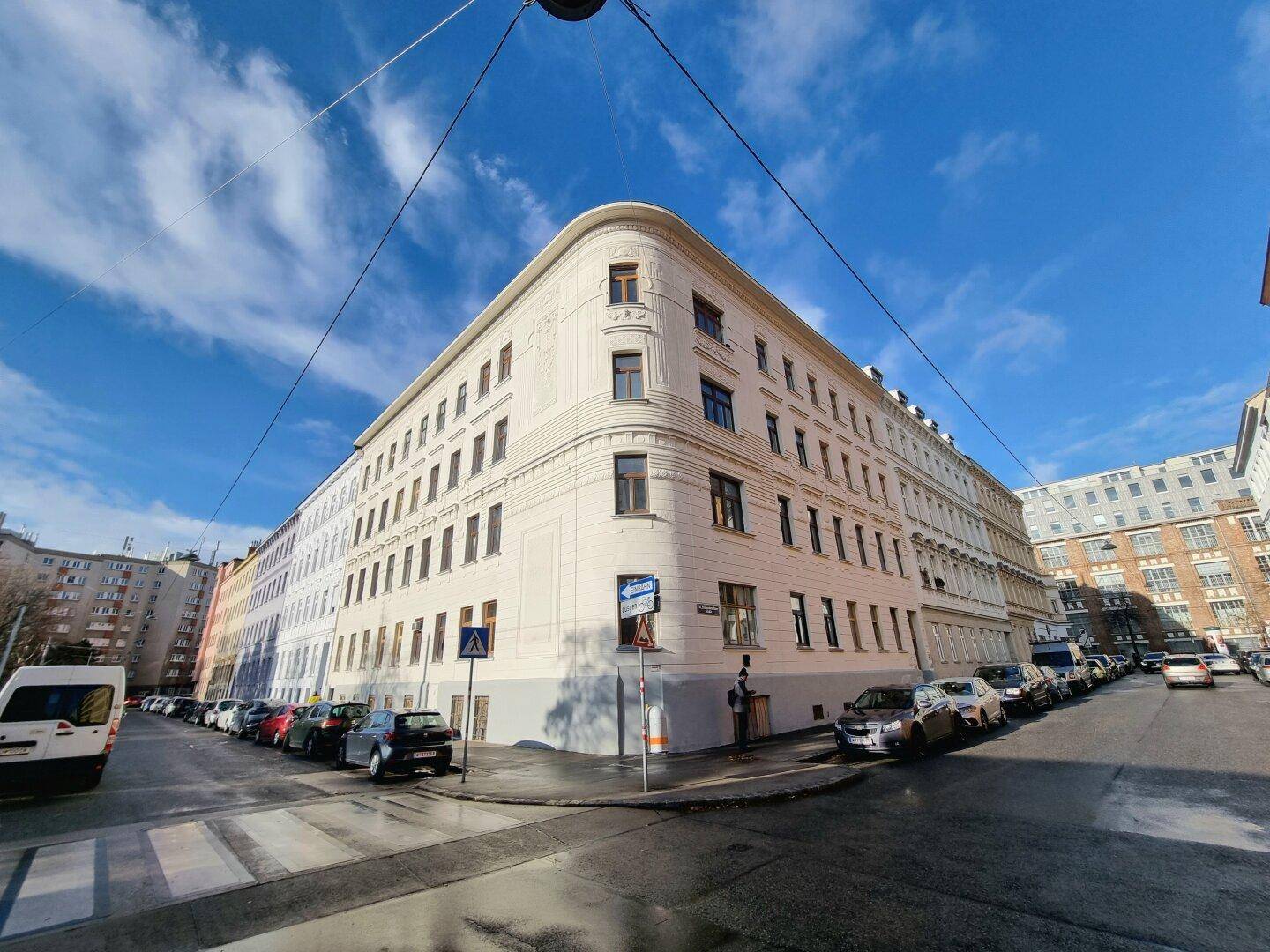 Weitläufige Ansicht des historischen Eckgebäudes unter blauem Himmel mit parkenden Autos.