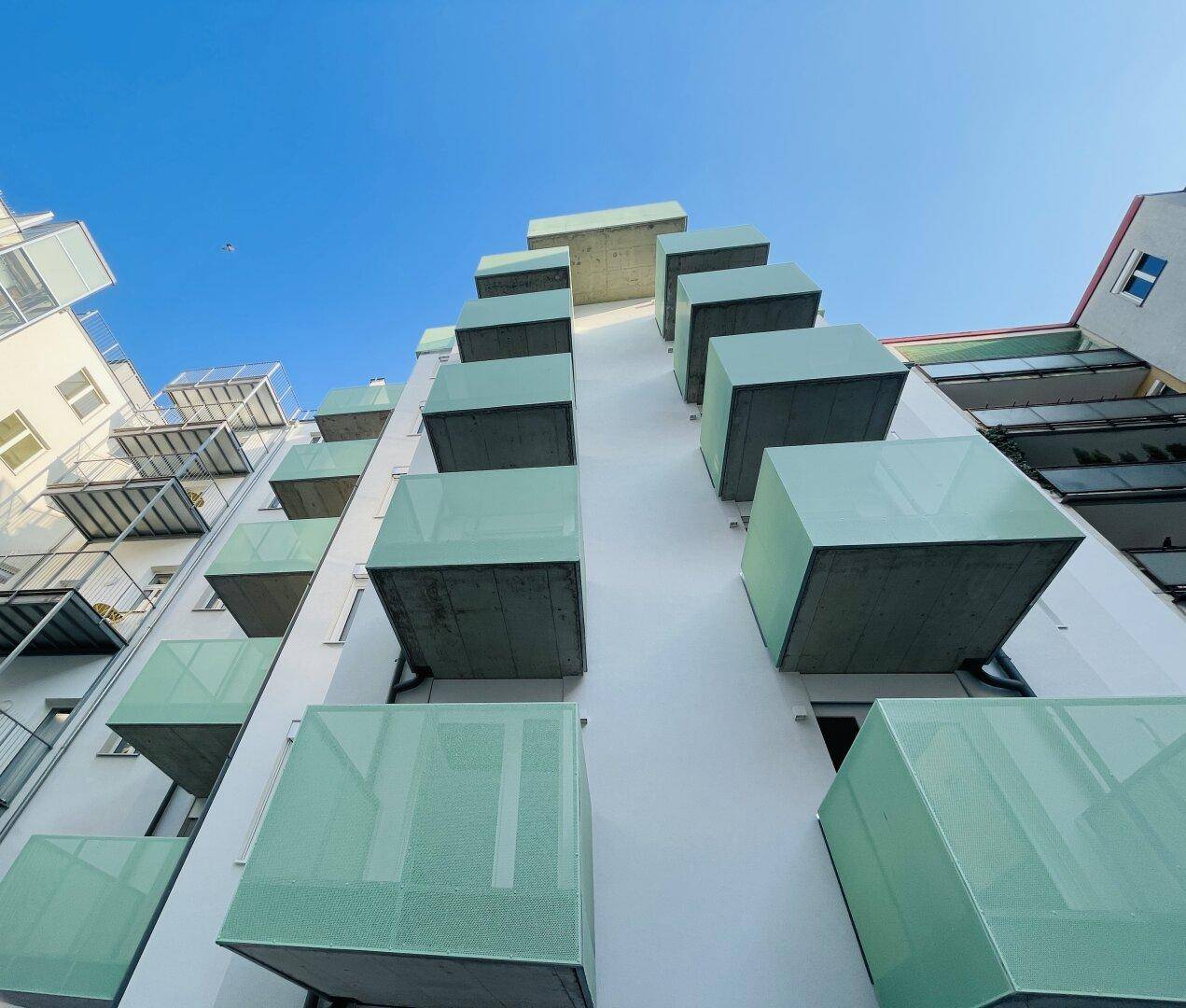 Moderne Wohnhausfassade mit vielen kleinen, würfelförmigen Balkonen unter blauem Himmel.