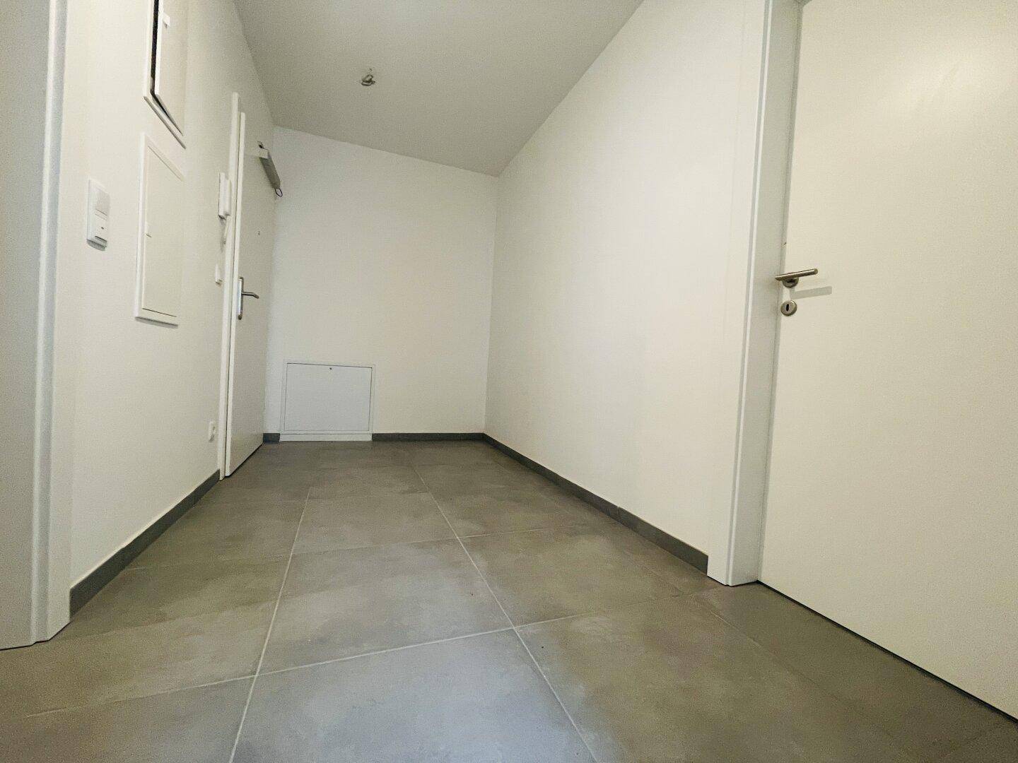 Heller Flur mit Fliesenboden und weißen Wänden, der zu verschiedenen Räumen führt.