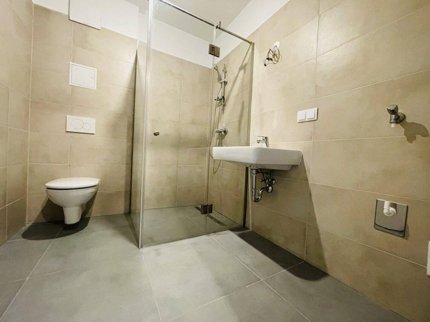 Modernes Badezimmer mit beigefarbenen Fliesen, ebenerdiger Dusche und wandhängendem WC.