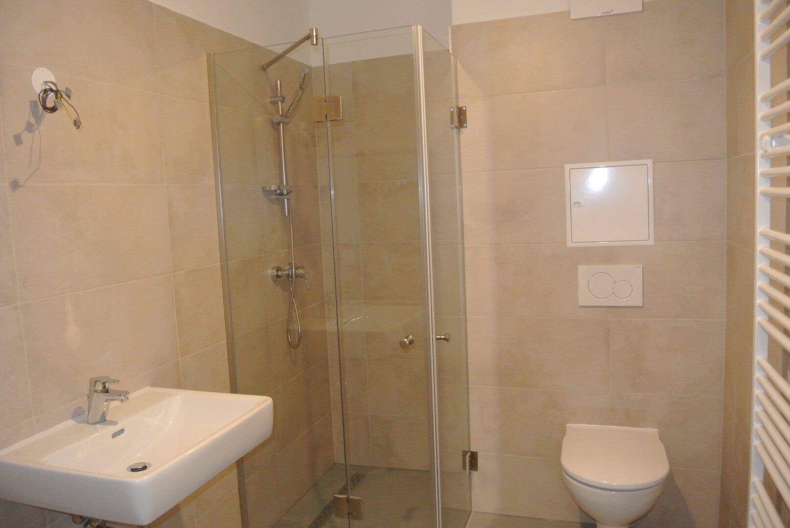 Modernes Badezimmer mit beigefarbenen Fliesen, Dusche und wandhängendem WC.