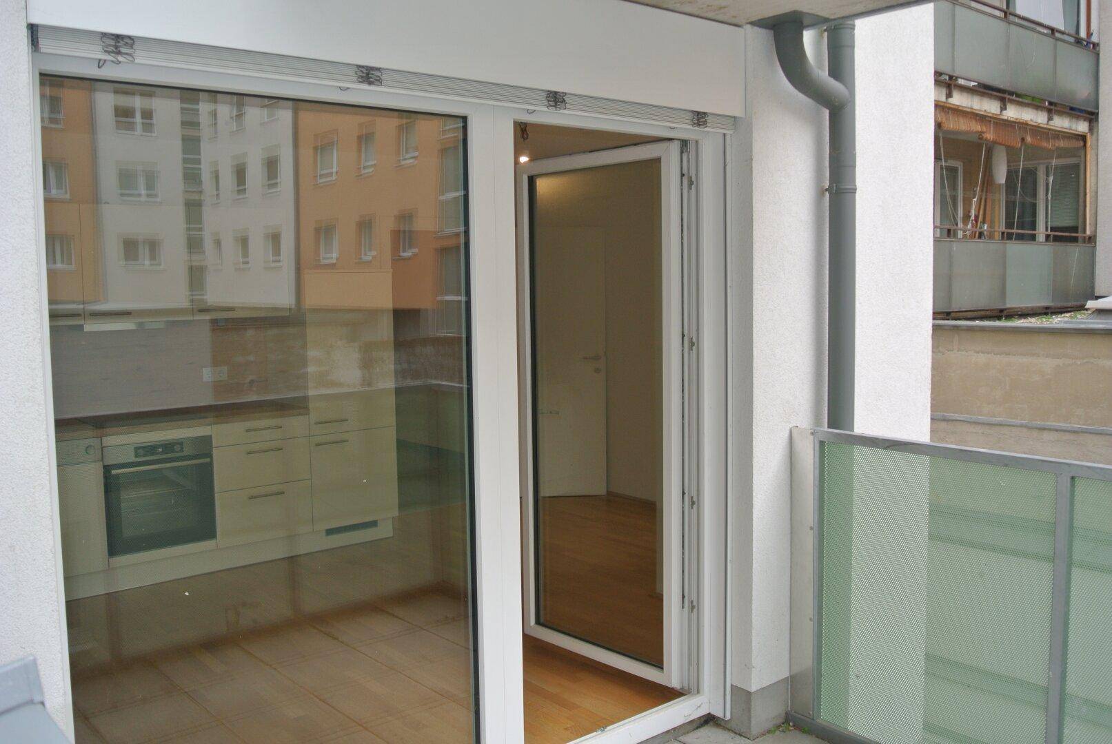Blick vom Balkon in eine helle Wohnung mit Holzboden und einer modernen Küche im Spiegelbild.